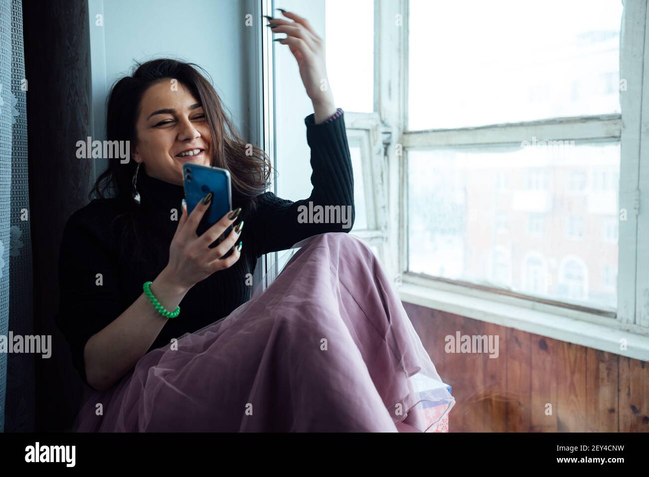 Ein deprimiertes Mädchen sitzt am Fenster und spricht weiter Das Telefon Stockfoto