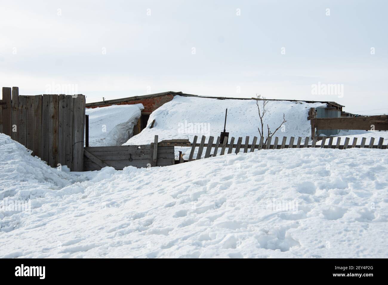 Altes Dorfhaus, alter Holzzaun, der während eines Schneesturms mit Schnee bedeckt ist. Das Haus ist nach einem Sturm oder starkem Schneefall mit Schnee bedeckt Stockfoto