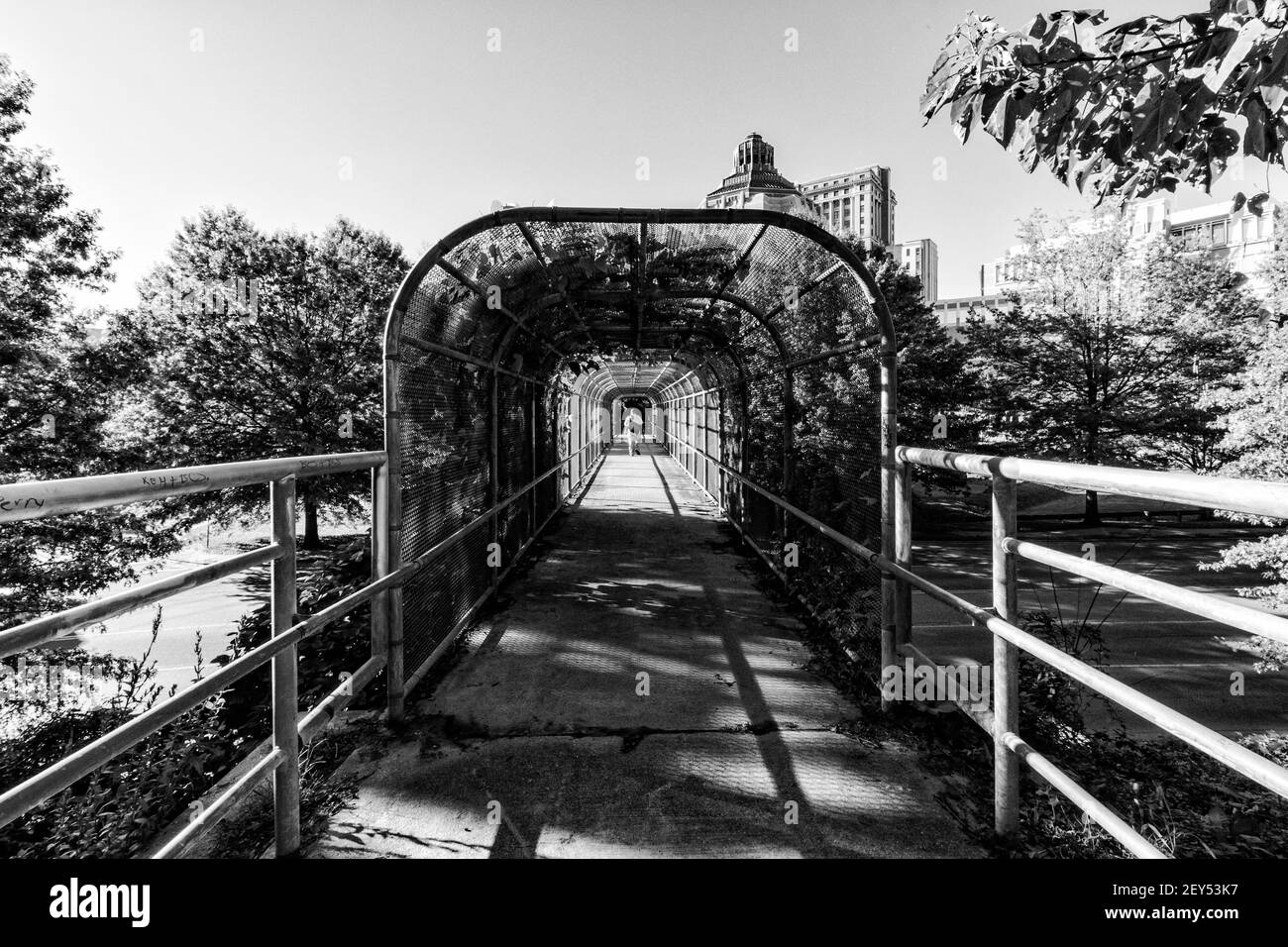 Ein Mann schreitet zur Arbeit an einer Fußgängerbrücke in Richtung Asheville, NC, USA, mit dem City Building gerade sichtbar auf der rechten Seite. Stockfoto