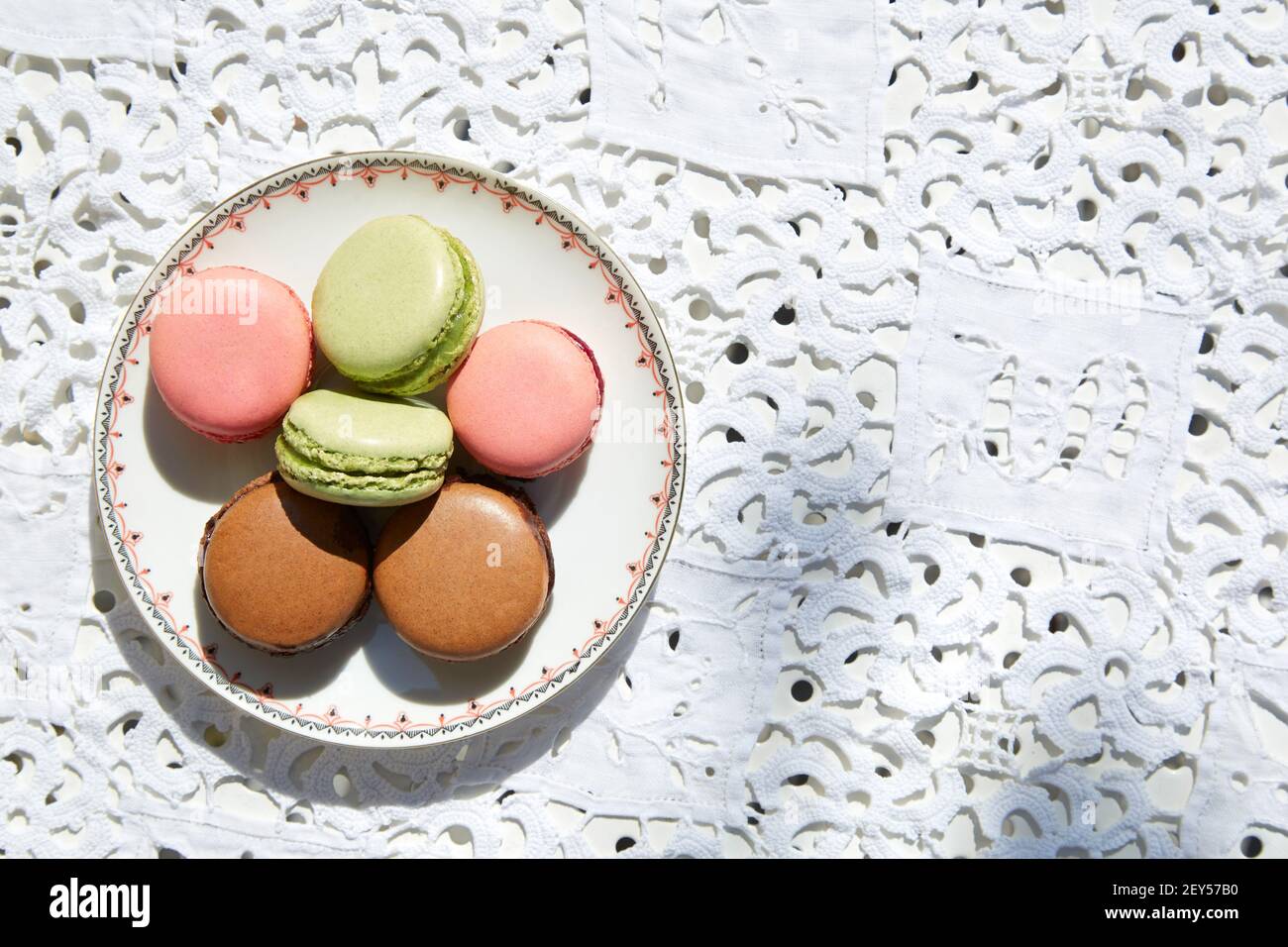 Makronen-Kekse in rosa, grün und braun mit Keramik-Untertasse, Draufsicht Stockfoto