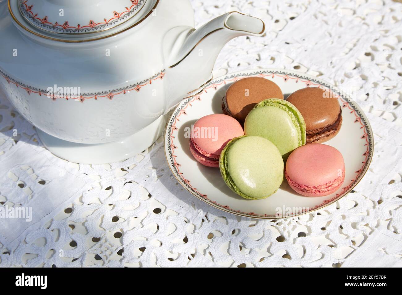 Makronen Kekse mit Keramik-Untertasse und Teekanne, weiß bestickte Tischdecke Stockfoto