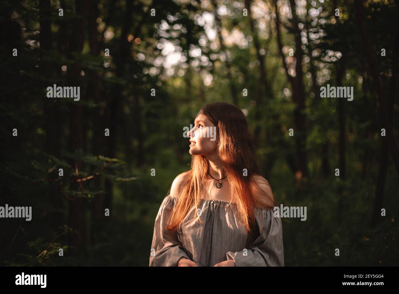 Junge Frau, die im dunklen Wald auf das Sonnenlicht schaut Stockfoto