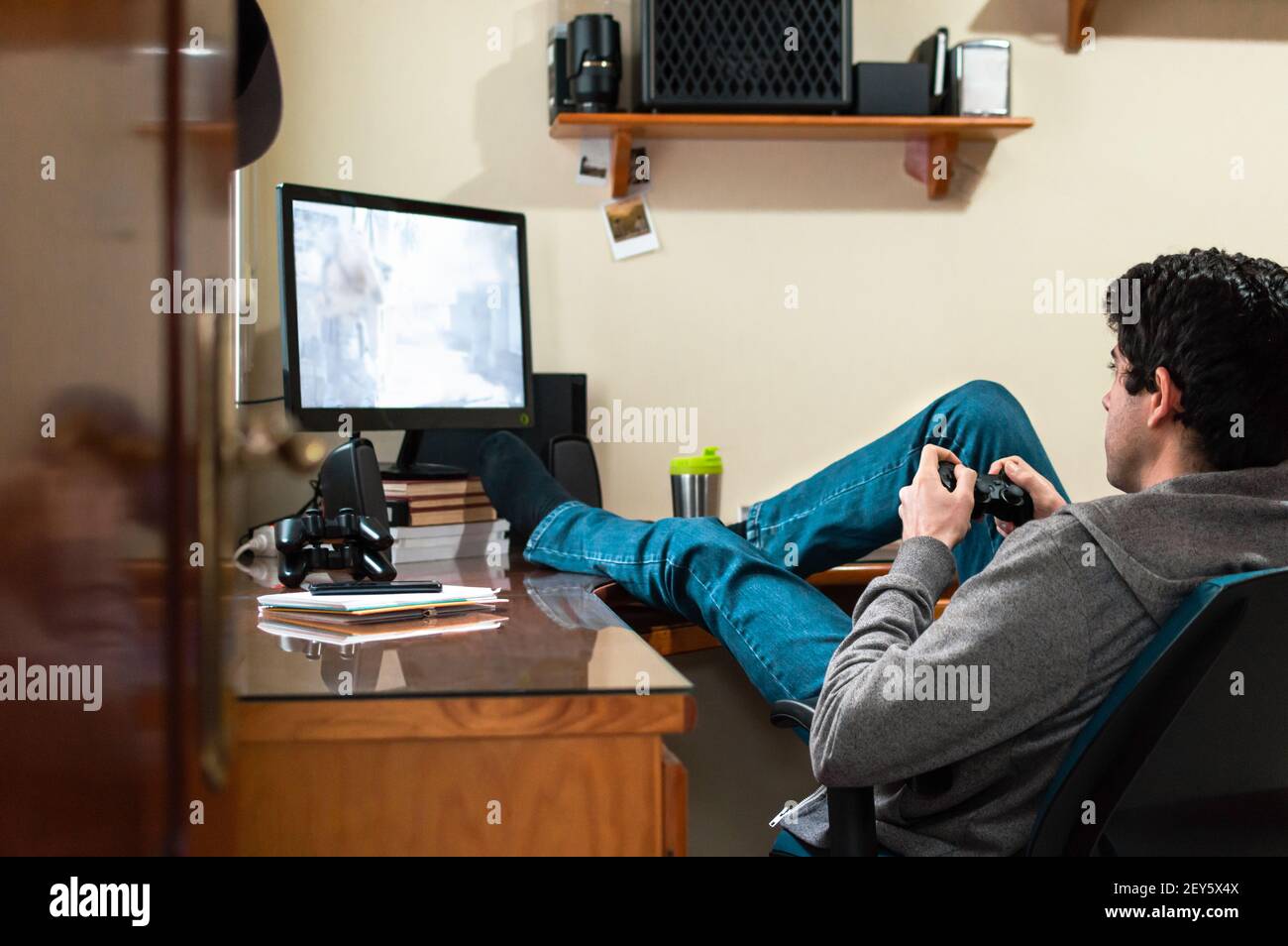 Junger Mann in Sweatshirt und Jeans entspannt spielen Videospiele in seinem Schlafzimmer. Stockfoto