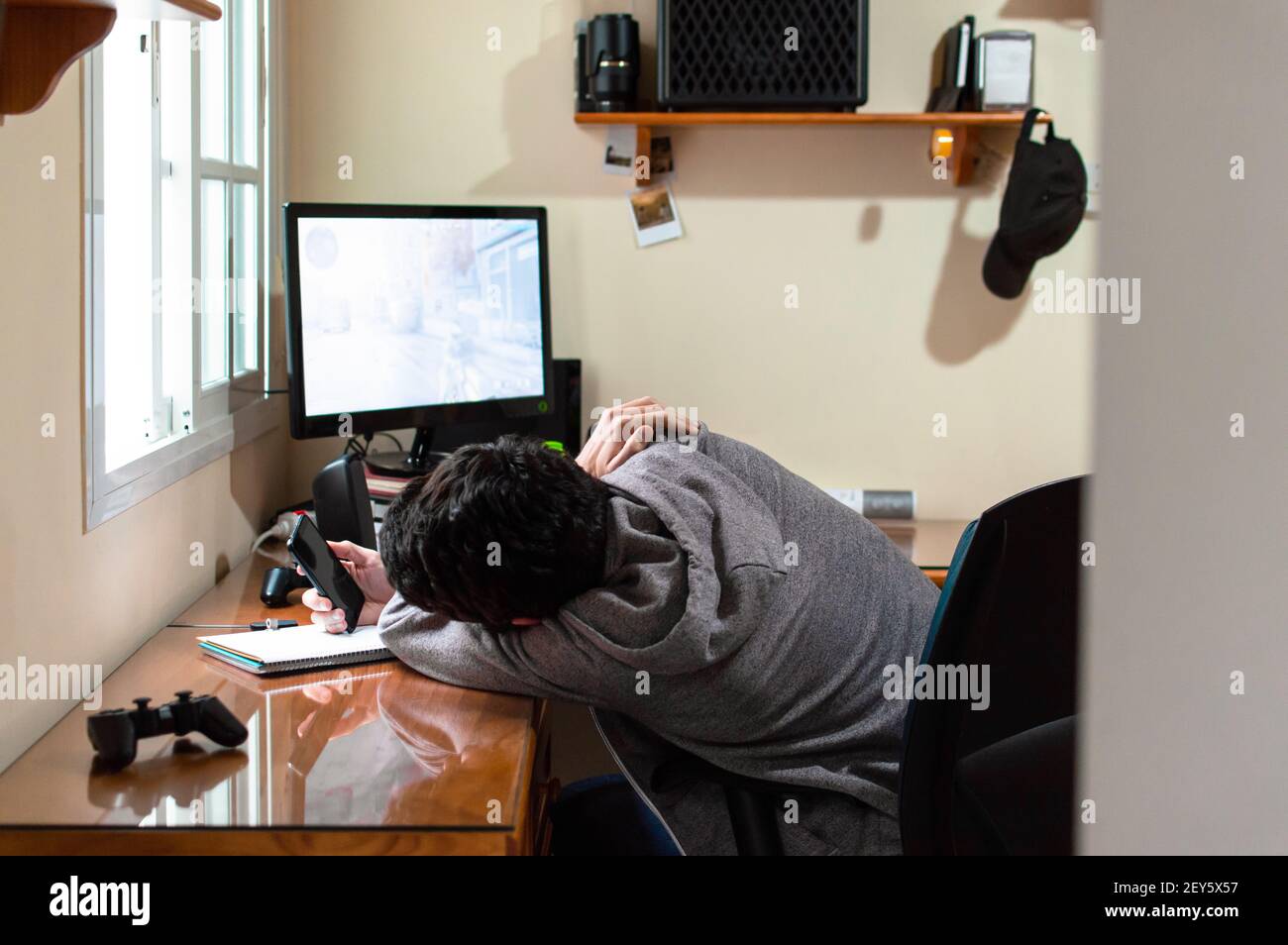 Gelangweilter Mann, der ein Telefon in einem Zimmer voll von benutzte Technologie an einem langen Tag Stockfoto