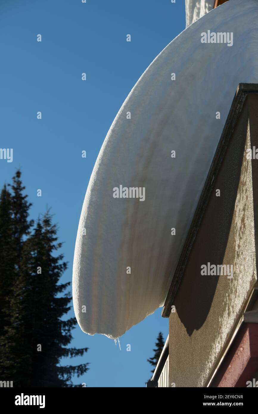 Schneelastenschichten, die vom Haus- oder Ski-Chalet-Dach hängen überhängender Schnee, der von schmelzenden Frost-Tautemperaturen abdriftet gefährliche Winterdachwartung Stockfoto