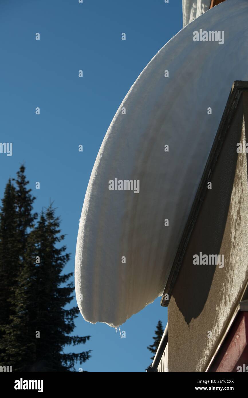 Schneelastenschichten, die vom Haus- oder Ski-Chalet-Dach hängen überhängender Schnee, der von schmelzenden Frost-Tautemperaturen abdriftet gefährliche Winterdachwartung Stockfoto