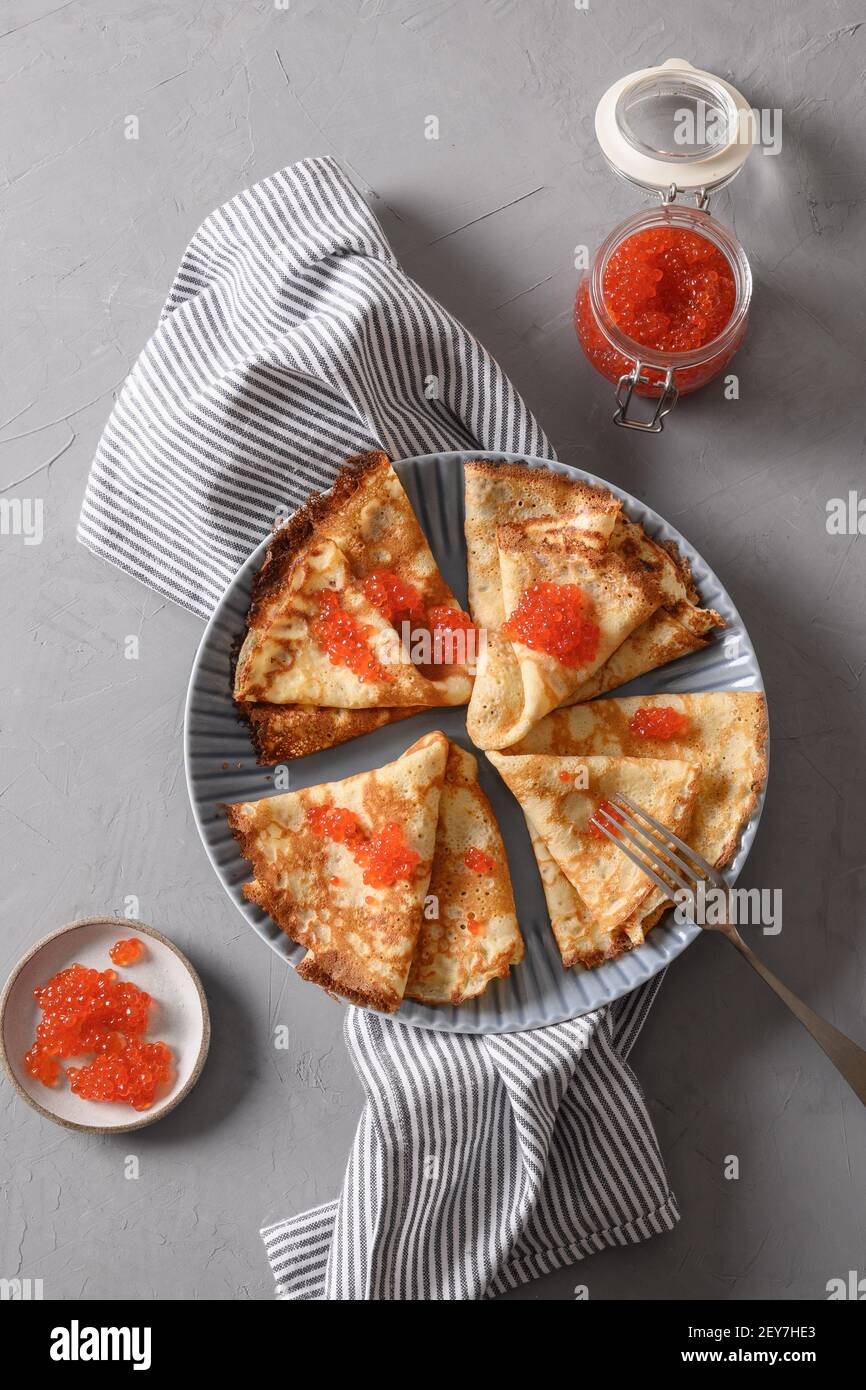 Russische dünne Pfannkuchen oder Blini mit rotem Kaviar auf grauem Teller. Draufsicht. Vertikales Format. Fasching. Stockfoto