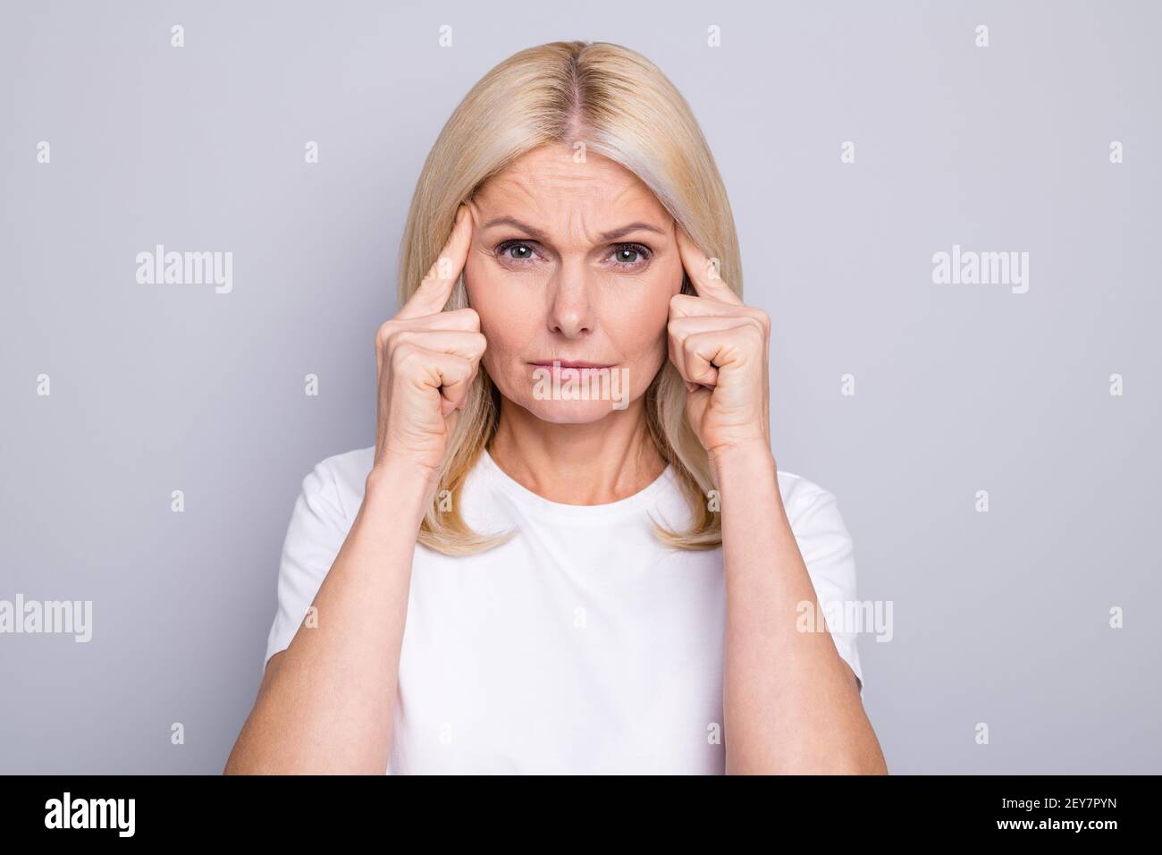 Foto von beunruhigten müde alte Dame Finger Tempel traurig aussehen Kamera tragen weißen T-Shirt isoliert grauen Hintergrund Stockfoto