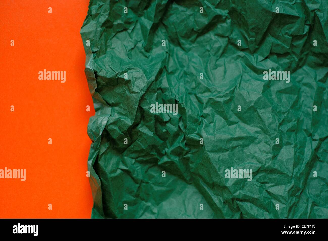 Leerer Papierhintergrund. Grün zerknittertes Papier auf einem orangen Hintergrund.Olive grün leeres Papier Hintergrund, Tapete, Ort für Text.Kreatives leeres Papier Stockfoto