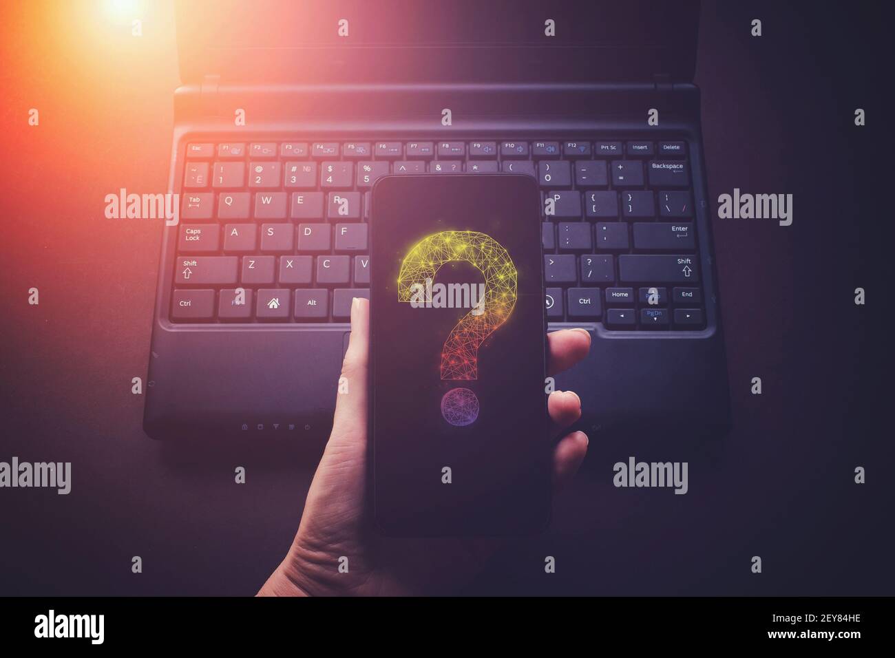 Hand halten Telefon mit Virtual low Poly Hologramm Fragezeichen auf Laptop Notebook Hintergrund, zukünftige Technologie Konzept Stockfoto