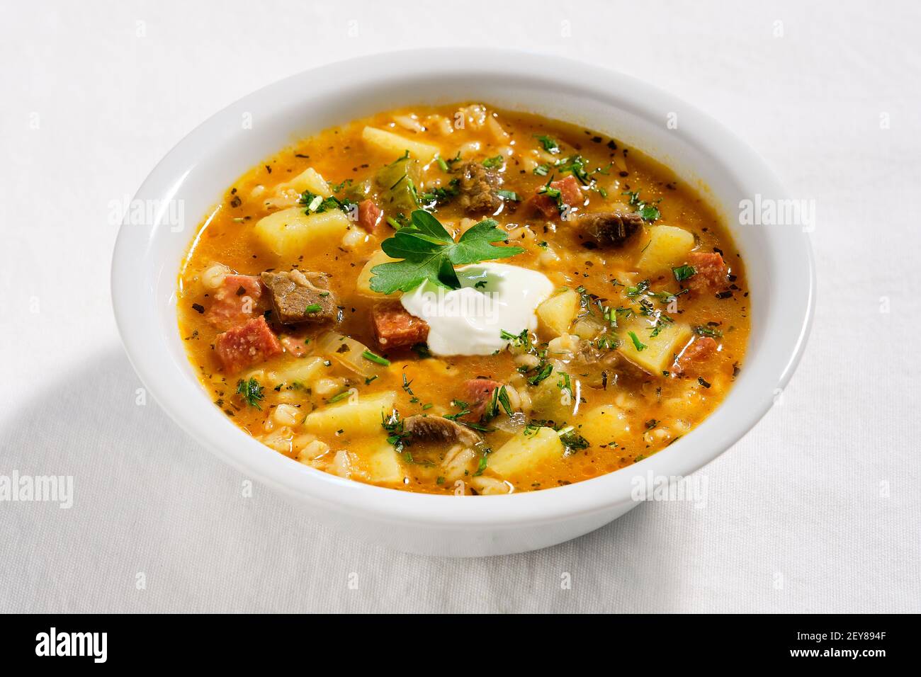 Rassolnik, Rind-, Gerste-, Karotten- und Gurkensuppe. Gekocht in salzig-saurer Gurkenbasis. Serviert in weißer Schale auf elfenbeinfarbener Stofftischdecke. Mit Stil Stockfoto