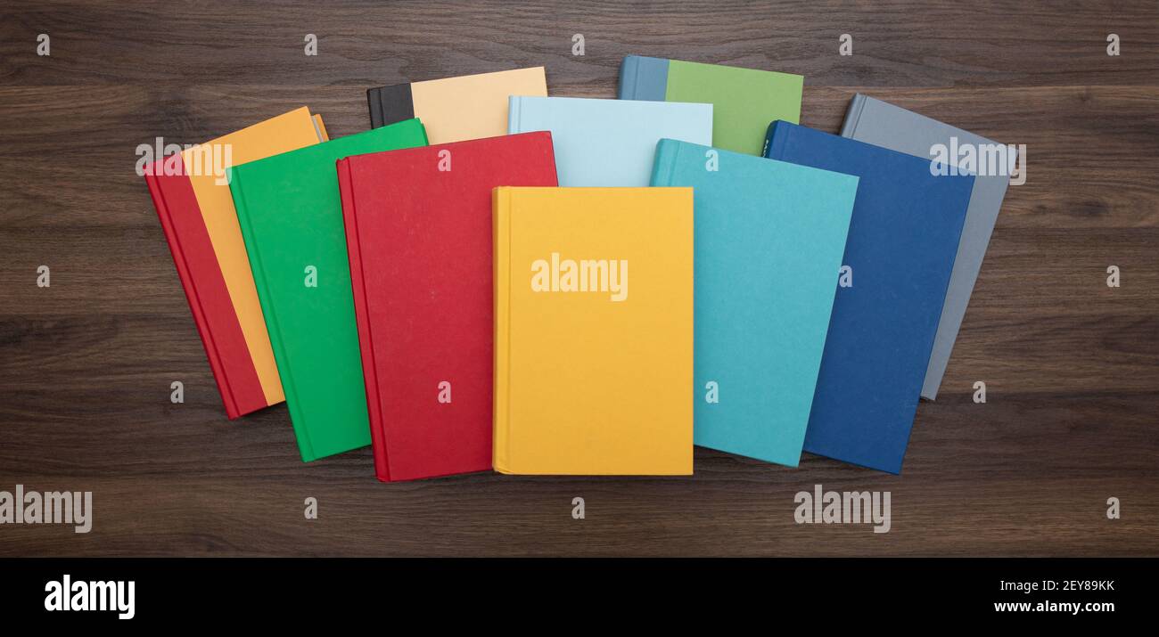 Draufsicht auf einen Stapel heller, farbenfroher Bücher, zentriert auf einem dunklen Schreibtisch. Stockfoto