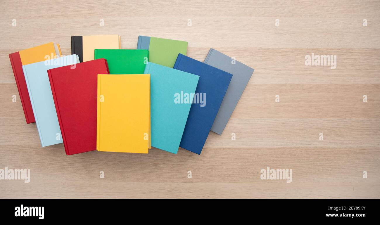 Draufsicht auf einen Stapel heller, farbenfroher Bücher auf einem hellen Holzschreibtisch mit Platz für Text. Stockfoto