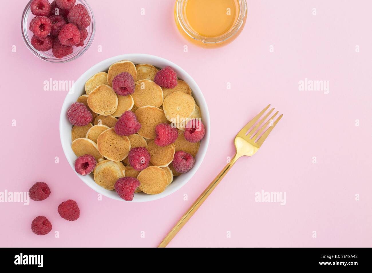 Draufsicht auf Mini-Pfannkuchen mit Himbeeren in weiß Schüssel auf der rosa Oberfläche Stockfoto
