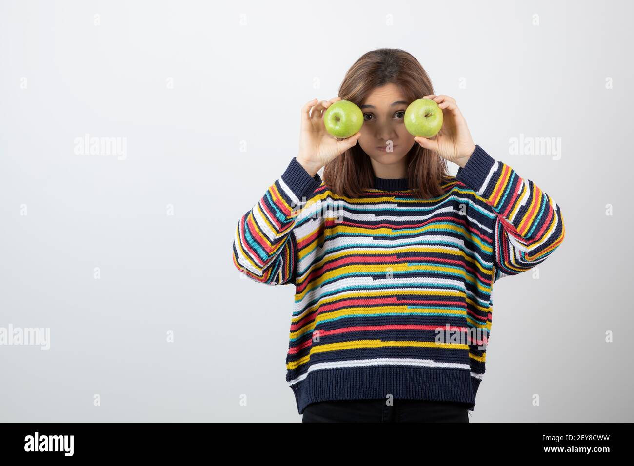 Junge Frau im lässigen Outfit hält grüne Äpfel vor Der Augen Stockfoto