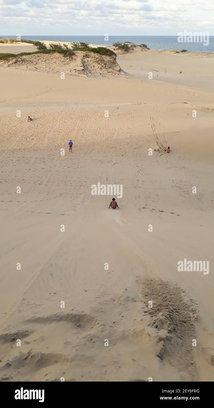 Die Leute, die am Strand den sandigen Hügel hinunter rutschen Im Sommer Stockfoto