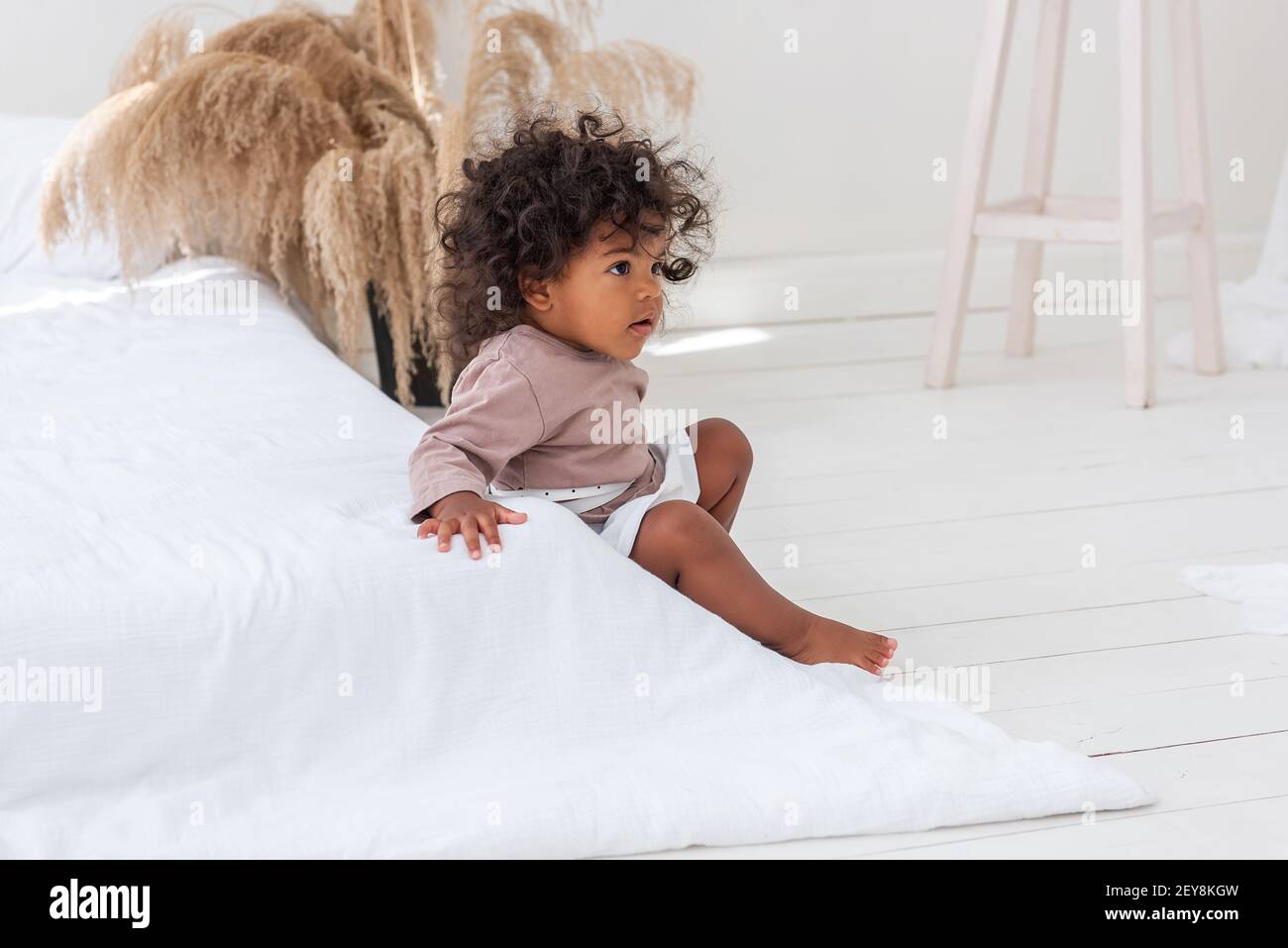 Kleine rothaarige afroamerikanische Mädchen spielt, läuft am weißen Bett, hat Spaß, lacht, lächelt. Das Konzept der Annahme multi-ethnischen Familie. Scandina Stockfoto