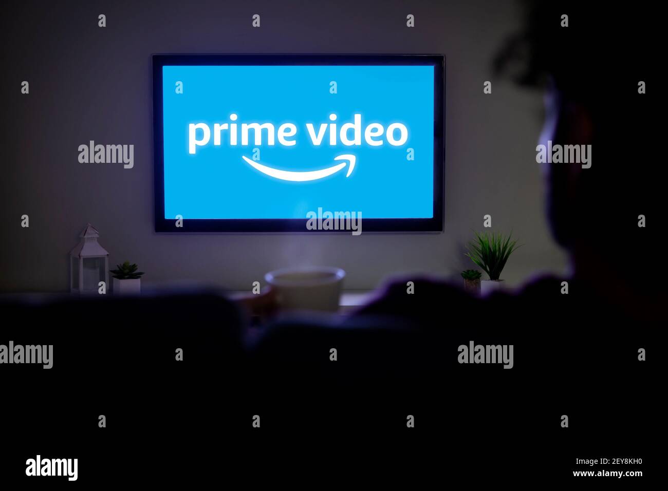 ROSARIO, ARGENTINIEN - 4. MÄRZ 2021: Amazon Prime Video-Logo auf dem Bildschirm von LED Smart TV. Afro-Mann beim Fernsehen zu Hause mit einer Kaffeetasse in der Hand. Stockfoto