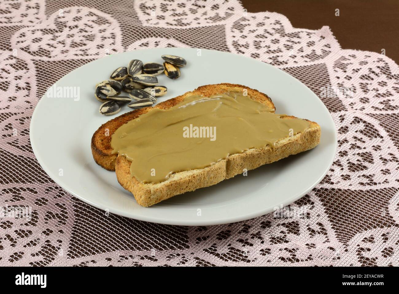 Sonnenblumenbutter auf Vollkornbrot mit Sonnenblumenkernen Auf weißem Teller die Sonnenblumenkerne auf Tischläufer aus Spitze aufrichten Stockfoto