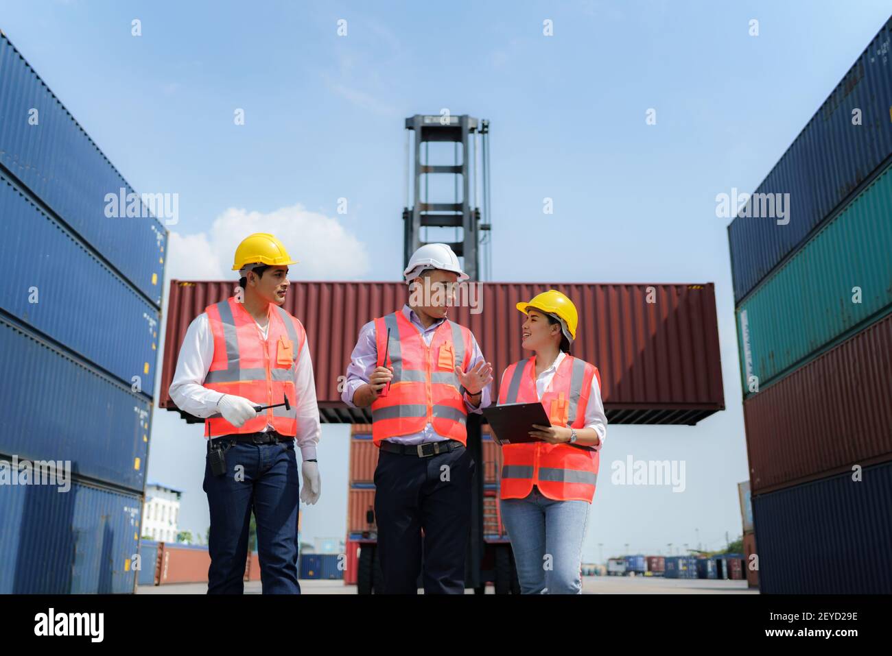 Asiatischer Vorarbeiter geht und erklärt den Arbeitern die verschiedenen Operationen im Containerdepot-Terminal. Stockfoto