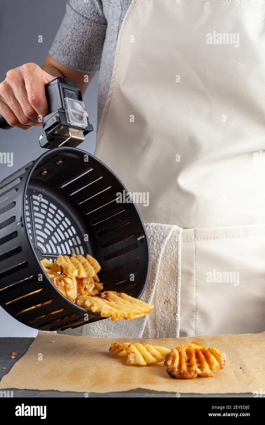 Eine Frau hält den Griff eines Ofenkorbs mit Frischkartoffeln mit hausgemachten frischen Waffeln im Inneren. Sie gießt sie auf Backpapier über k Stockfoto