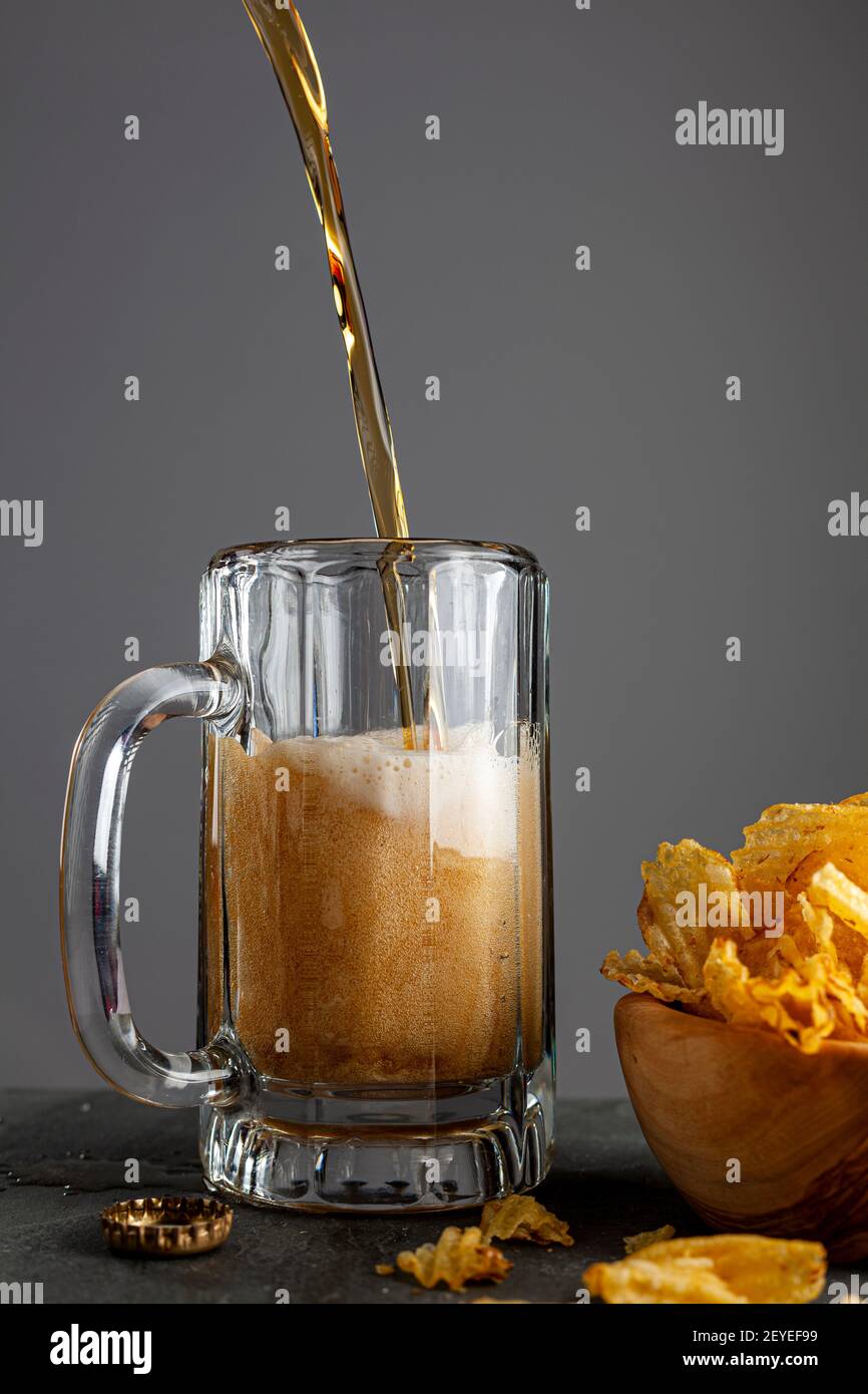 Craft Beer wird in einem Glas Becher mit Griff in einem Pub mit dunklem Hintergrund gegossen. Es schäumt und macht funkelt, wie das Glas füllt sich. Es gibt einen Arbeitsauftrag Stockfoto