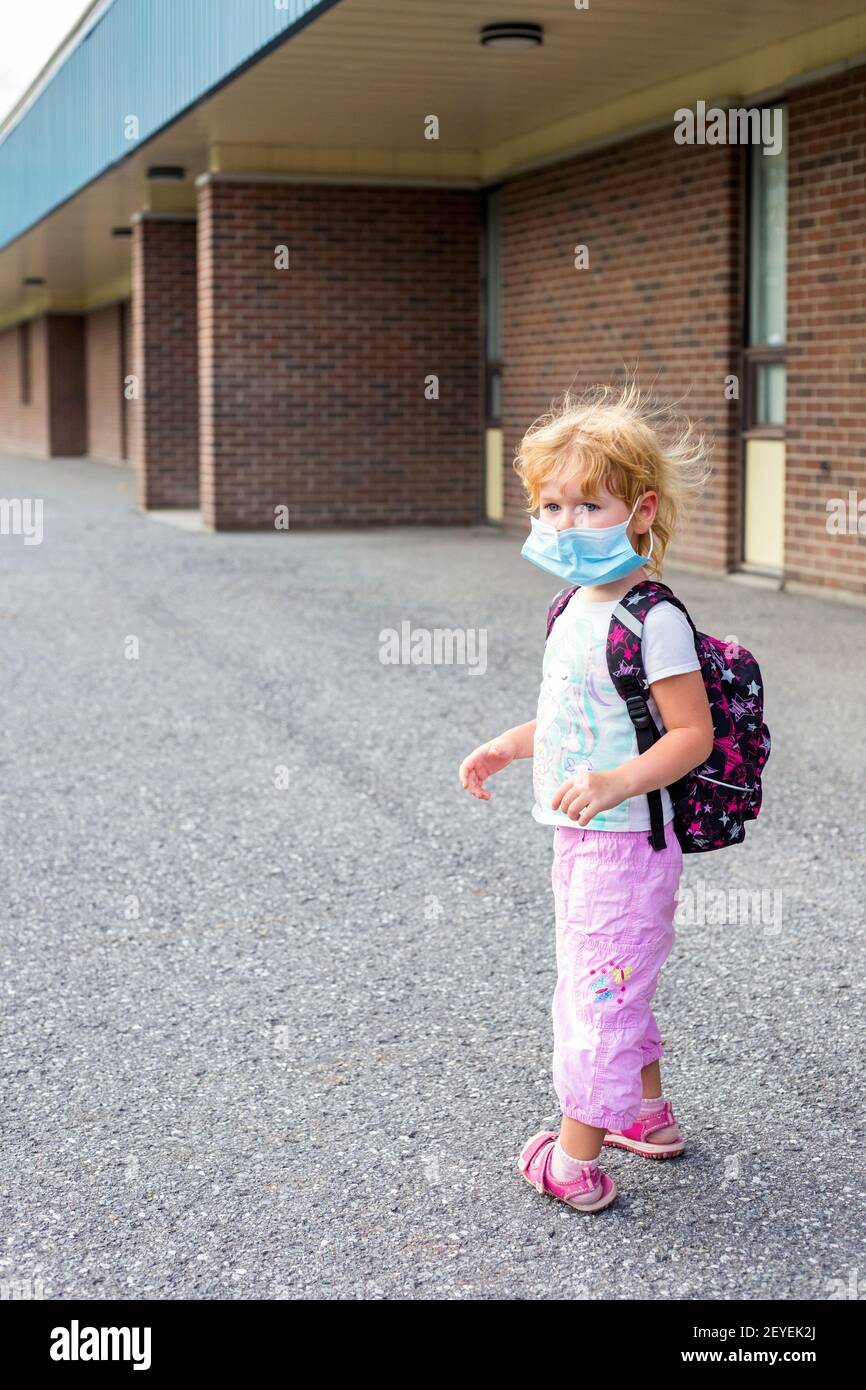 Kleine Vorschulkinder in Maske mit Rucksack während Corona Virus in der Nähe von Schulgebäude, in die Schule oder Kindergarten. Erster Schultag Konzept. Stockfoto