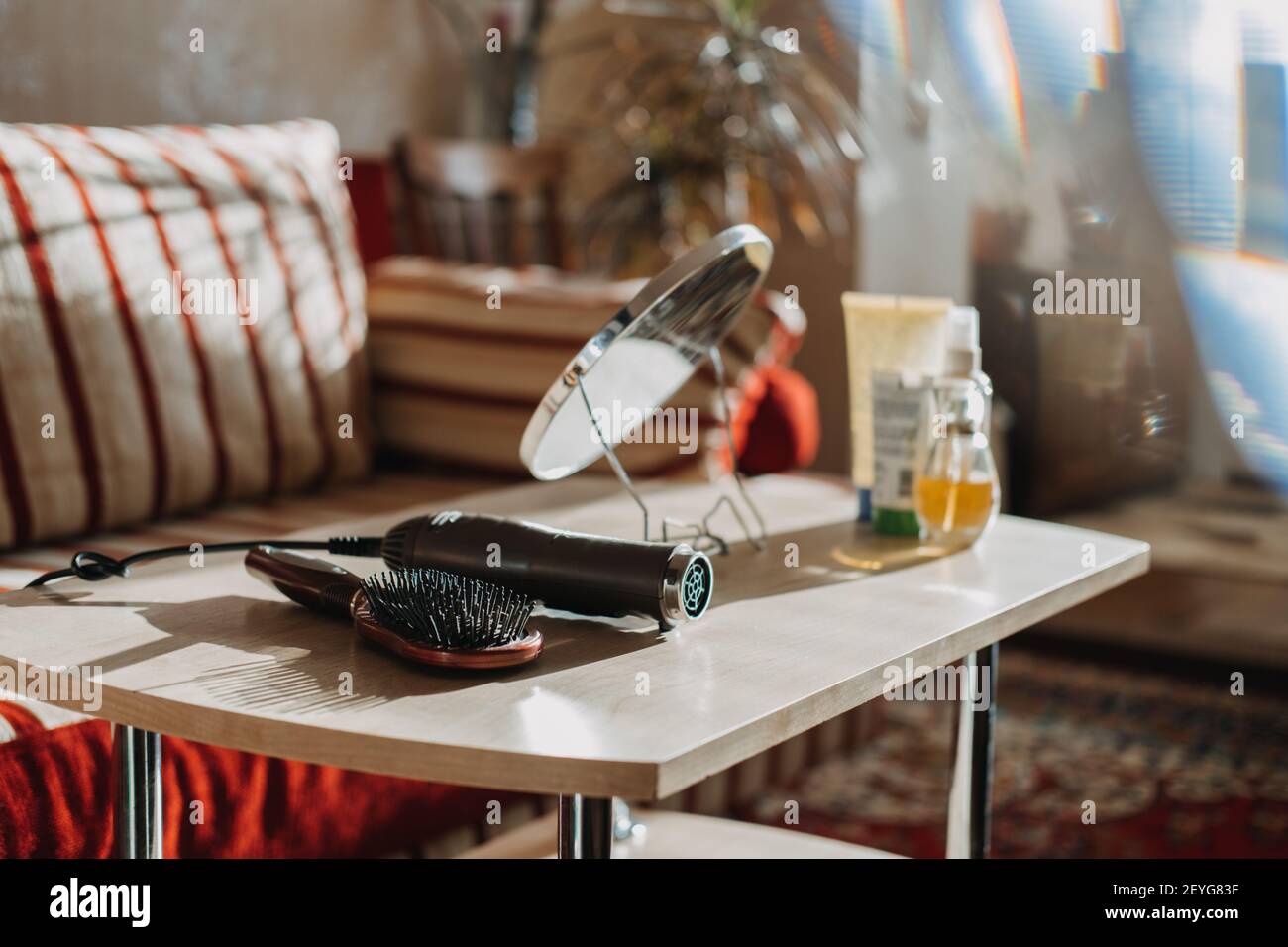 Haare zu Hause stylen. Styling und Behandlungen zu Hause. Kamm und Haartrockner sind auf dem Tisch vor dem Hintergrund von Kosmetikflaschen Stockfoto