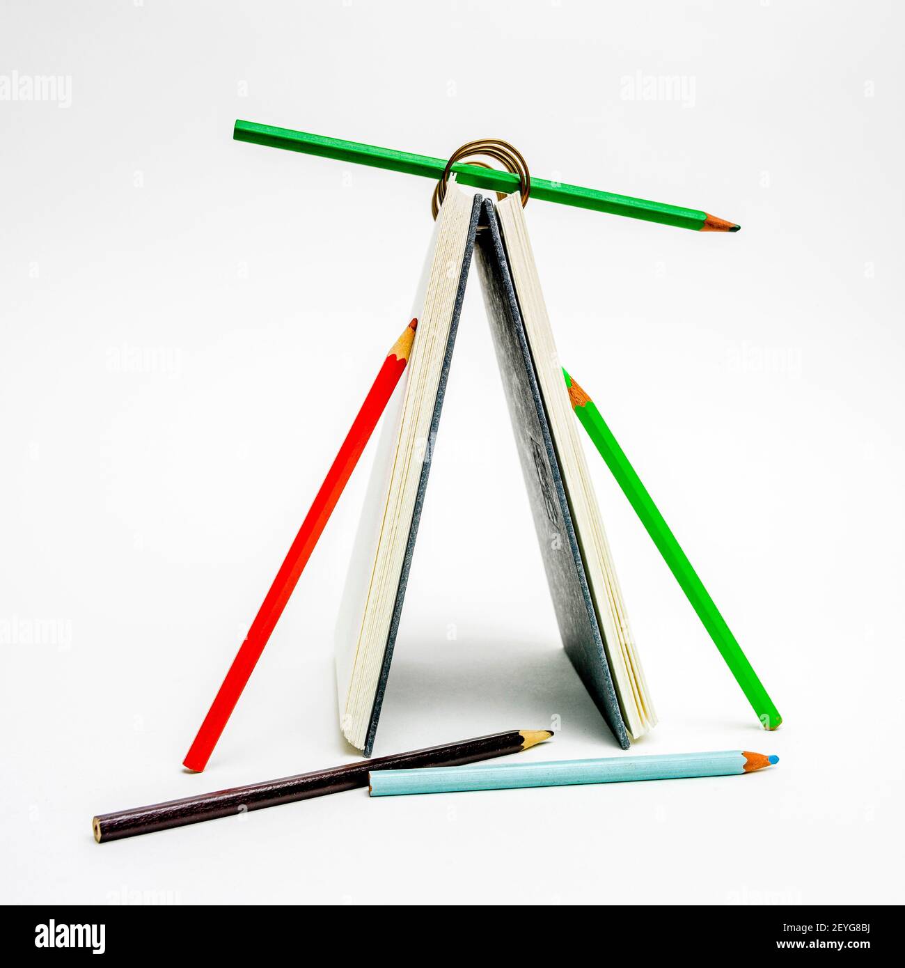 Kreative Anordnung eines Notizbuchs und Farbstiften, die eine einzigartige Struktur auf weißem Hintergrund bilden Stockfoto