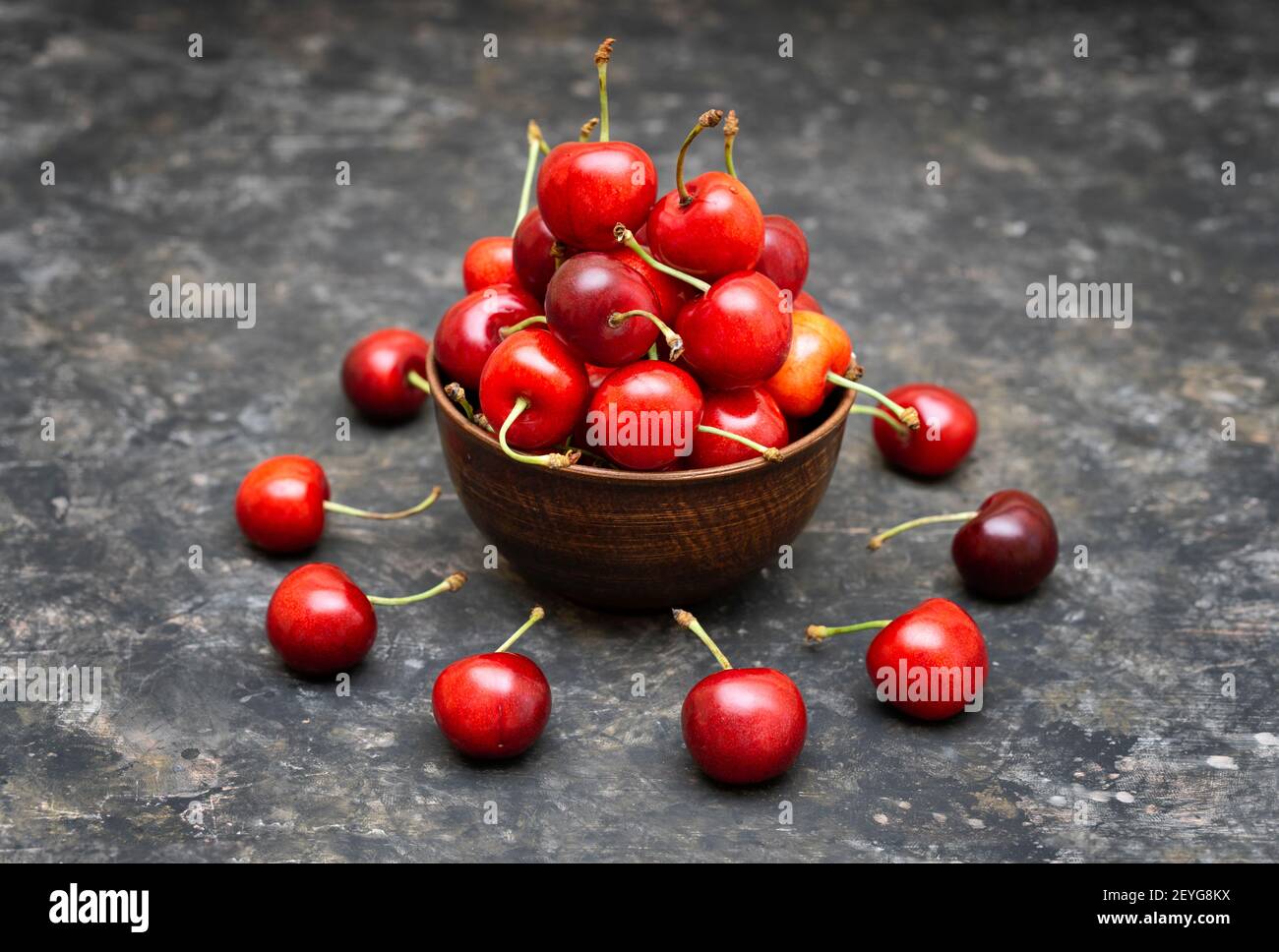 Holzschale voller Kirschen. Einige reife Früchte liegen um die Schüssel auf dem grungigen Tisch herum. Stockfoto