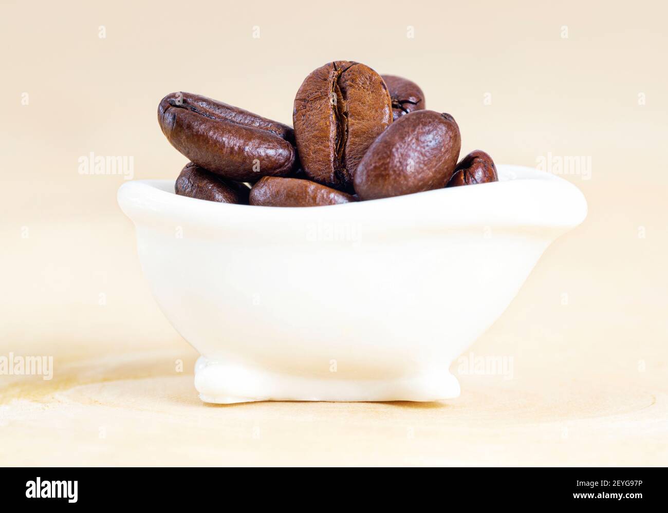 Nahaufnahme einer winzigen weißen Badewanne mit gerösteten Kaffeebohnen auf neutralem Hintergrund. Studioaufnahme, selektiver Fokus. Stockfoto