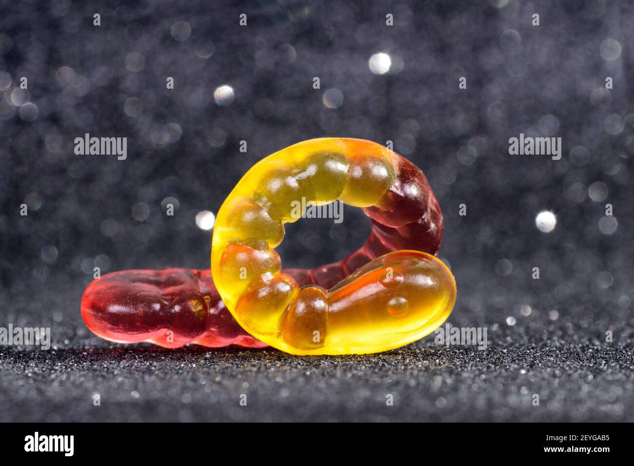Nahaufnahme eines gewellten gelb-roten Gummiwurms auf einem glitzernden unscharfen Hintergrund. Stockfoto