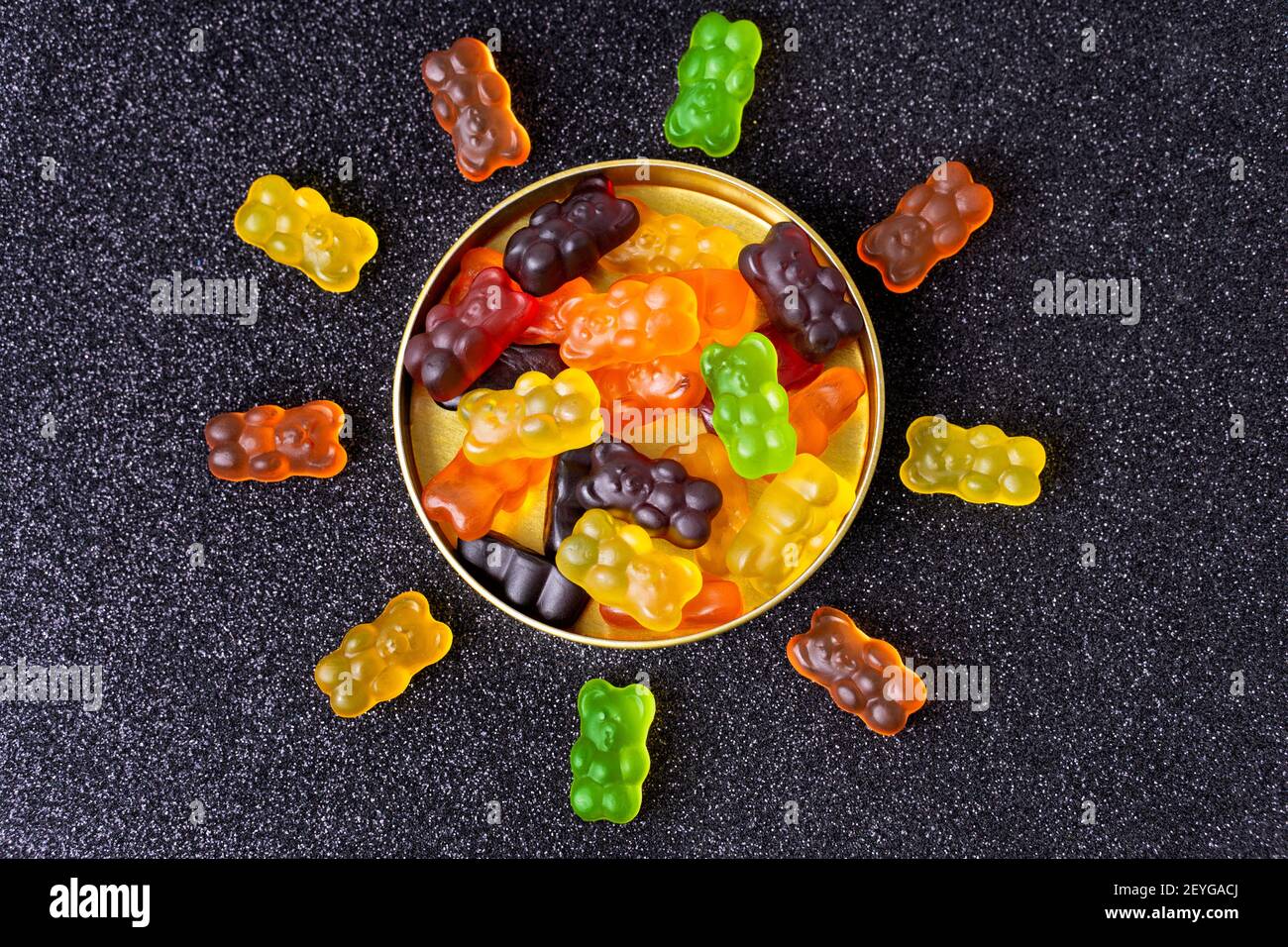 Gummibären in Form einer Sonne um eine Süßigkeitenkiste auf einem mit Zucker überzogenen Hintergrund angeordnet. Stockfoto