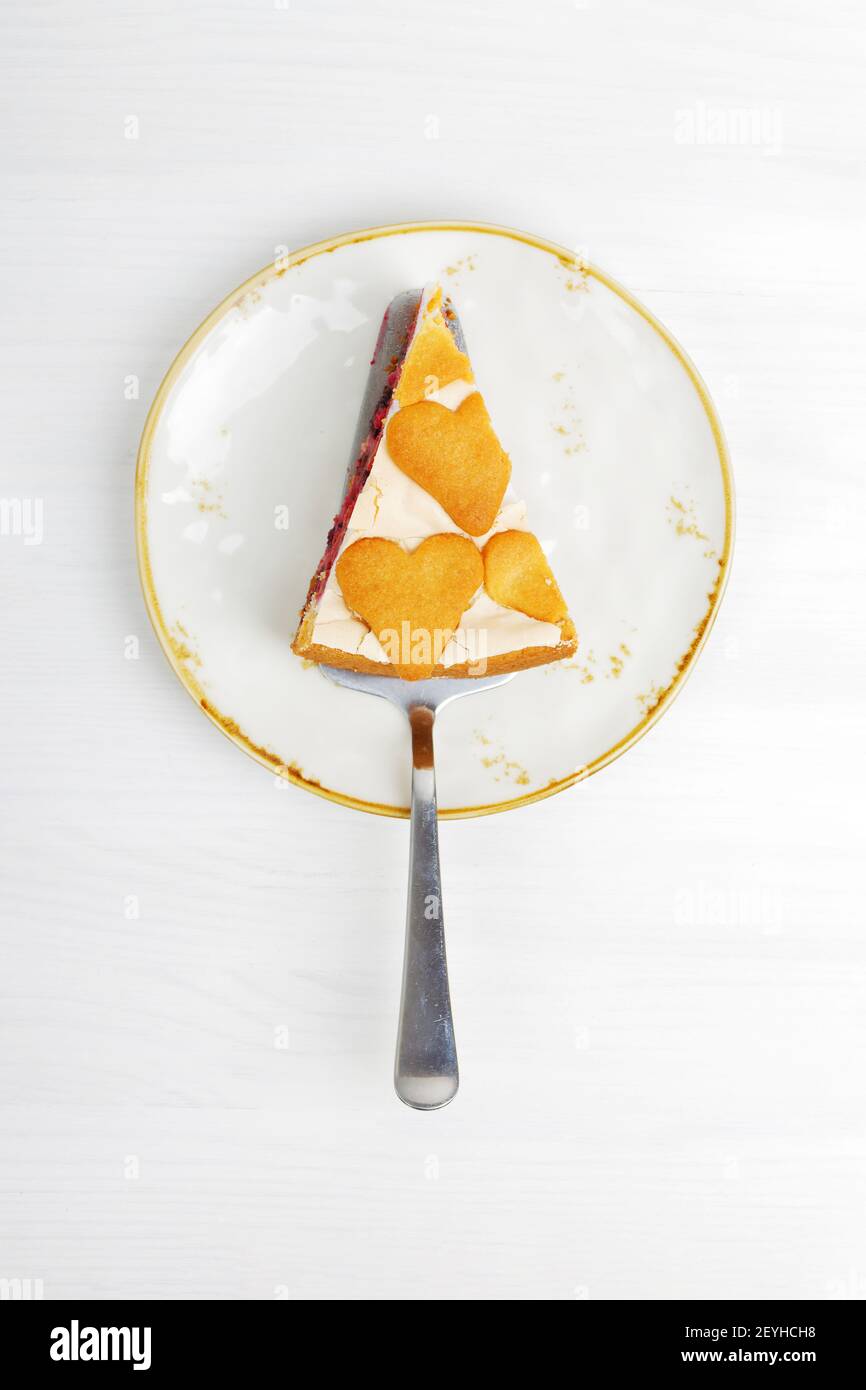 Stück hausgemachter Beerenkuchen mit Baiser und herzförmigen Plätzchen auf weißem Holztisch. Draufsicht. Stockfoto