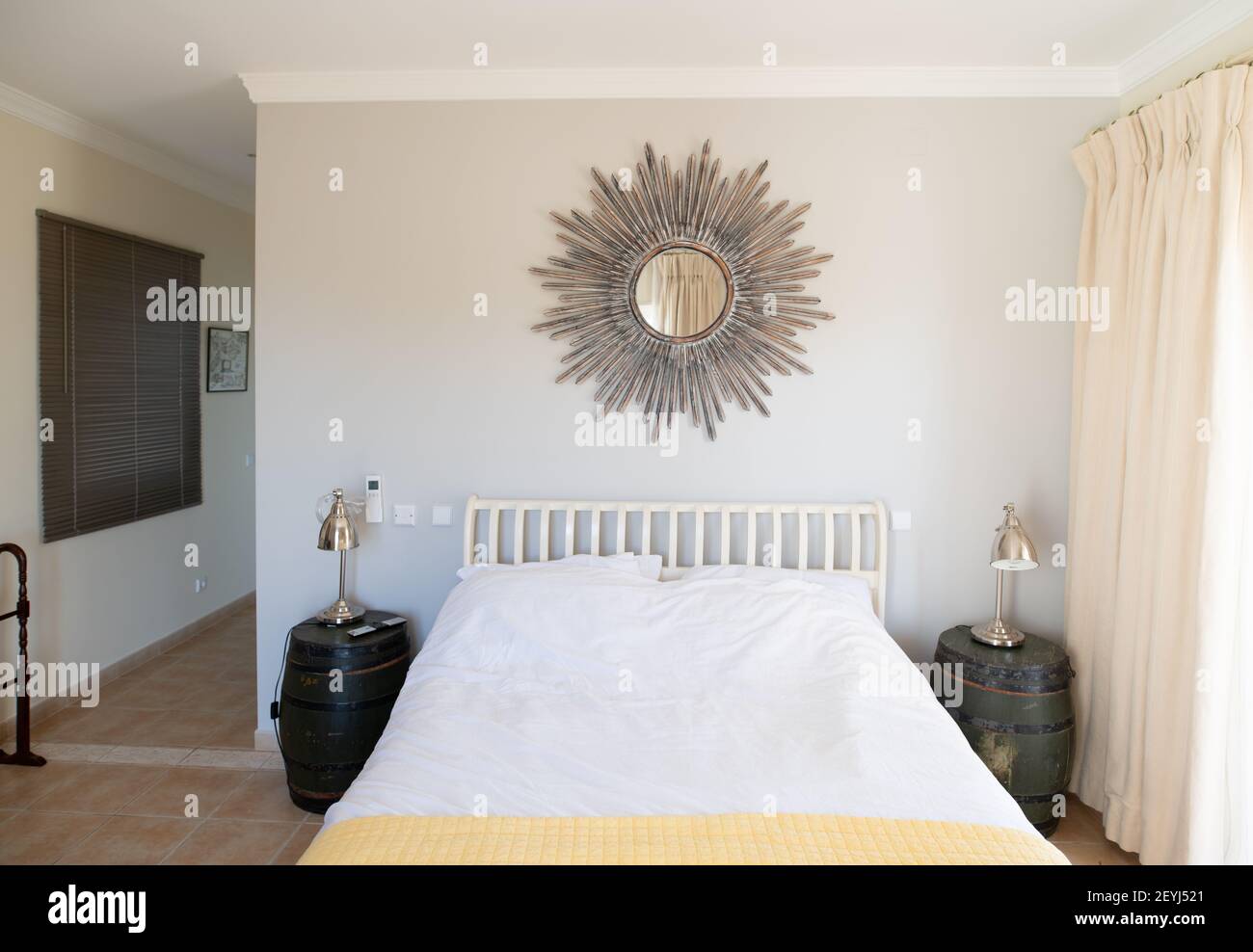 Einfaches Schlafzimmer mit verziertem Sonnenspiegel über einem weißen Doppelbett Bett Stockfoto