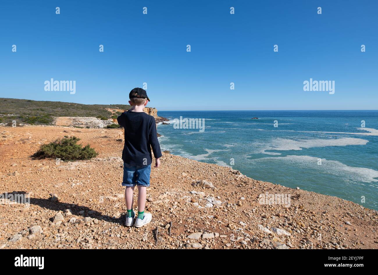 Kleiner Junge, der auf einem Küstenwanderweg steht und zu dem er hinschaut Meer Stockfoto