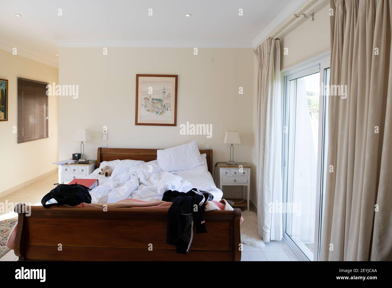 Algarve, Portugal; November 2020: Ein unordentliches Schlafzimmer mit ungefertigten Betten, Glasschiebetüren und viel Tageslicht Stockfoto