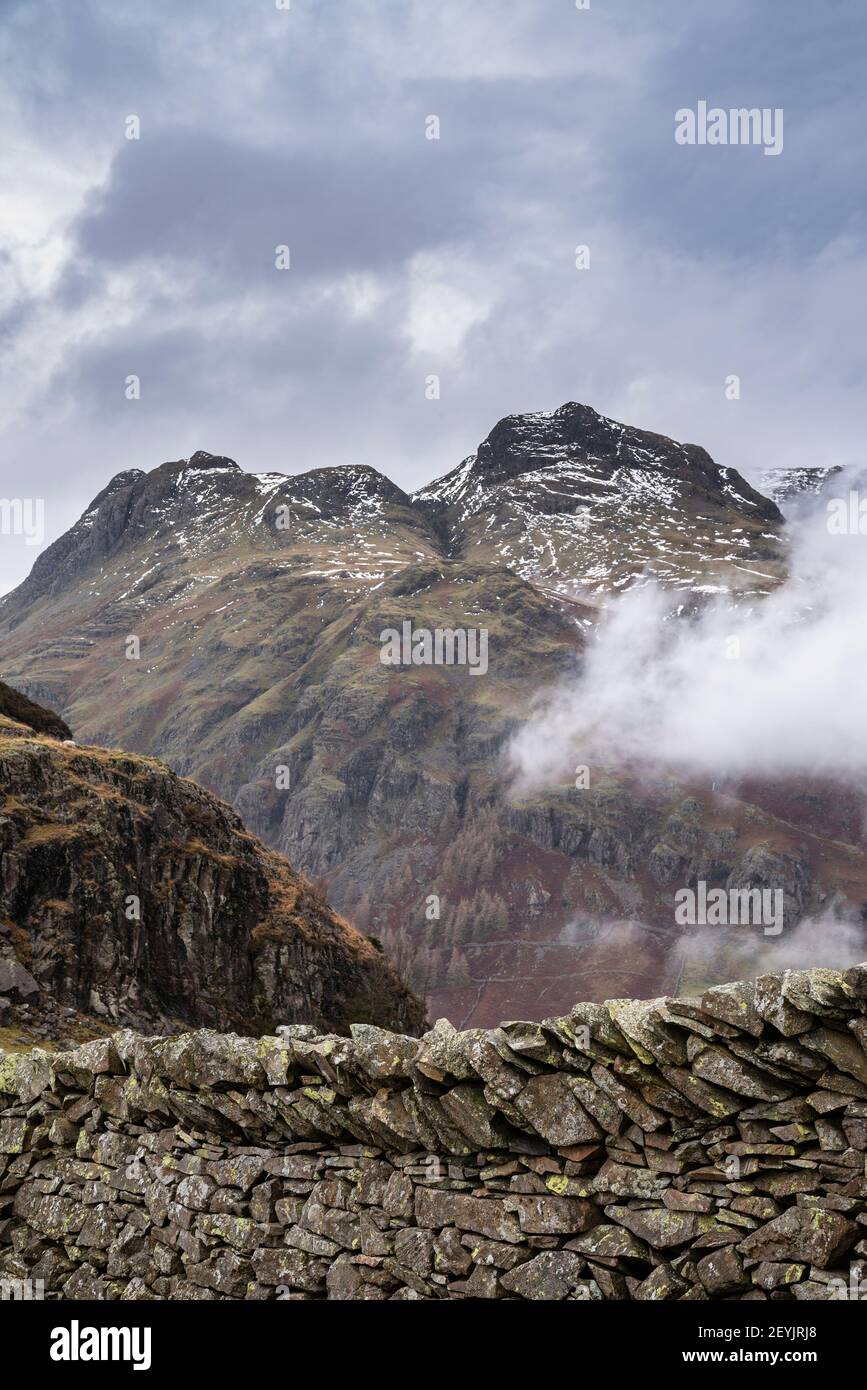 Atemberaubende Winterlandschaft Bild der Ansicht von Side Pike in Richtung Langdale Hechte mit niedrigen Wolken auf Bergspitzen und moody Mist Stockfoto