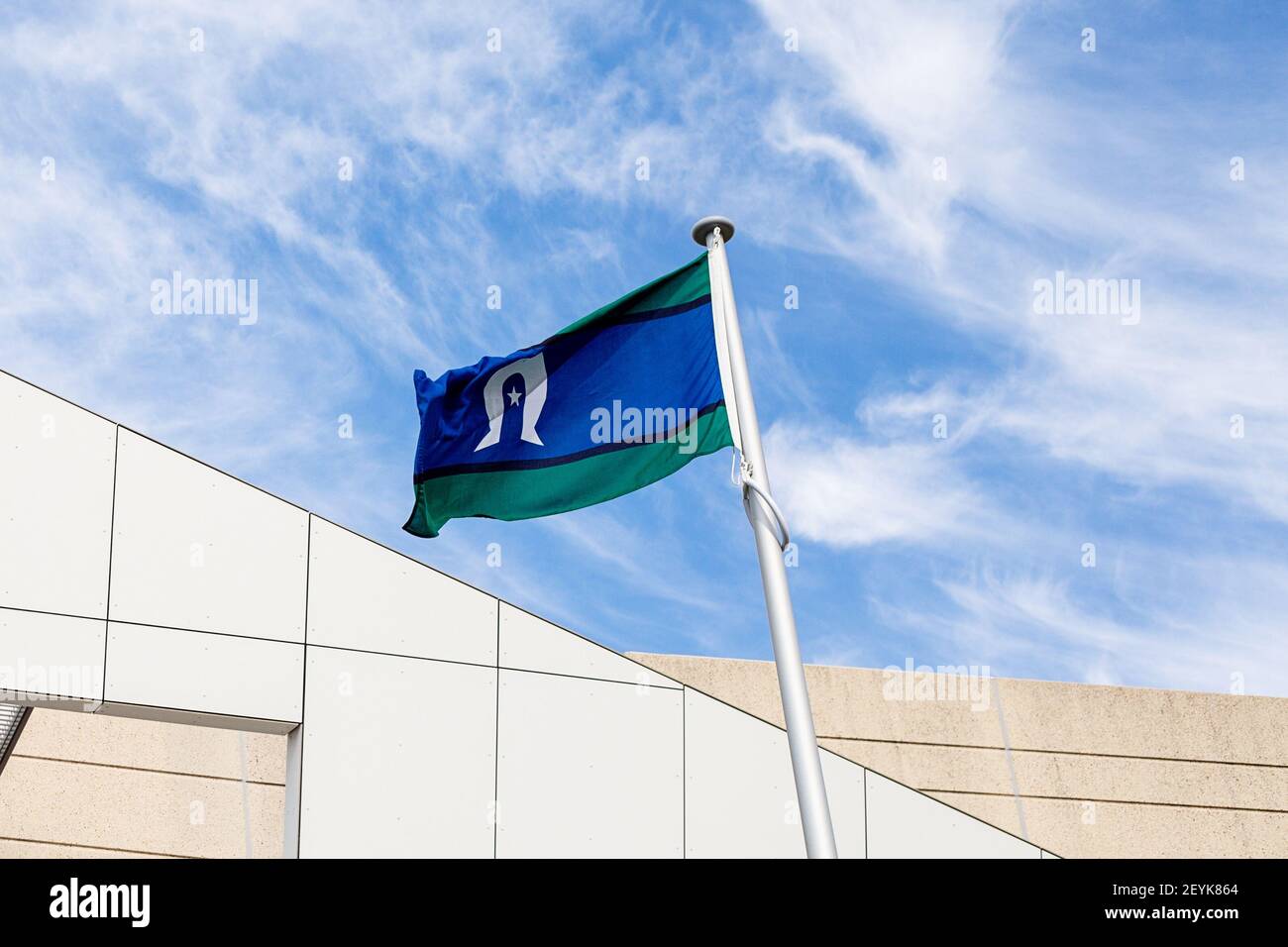Eine Torres Strait Islander Flagge, die gegen ein modernes Gebäude gegen einen bewölkten Himmel fliegt. Stockfoto