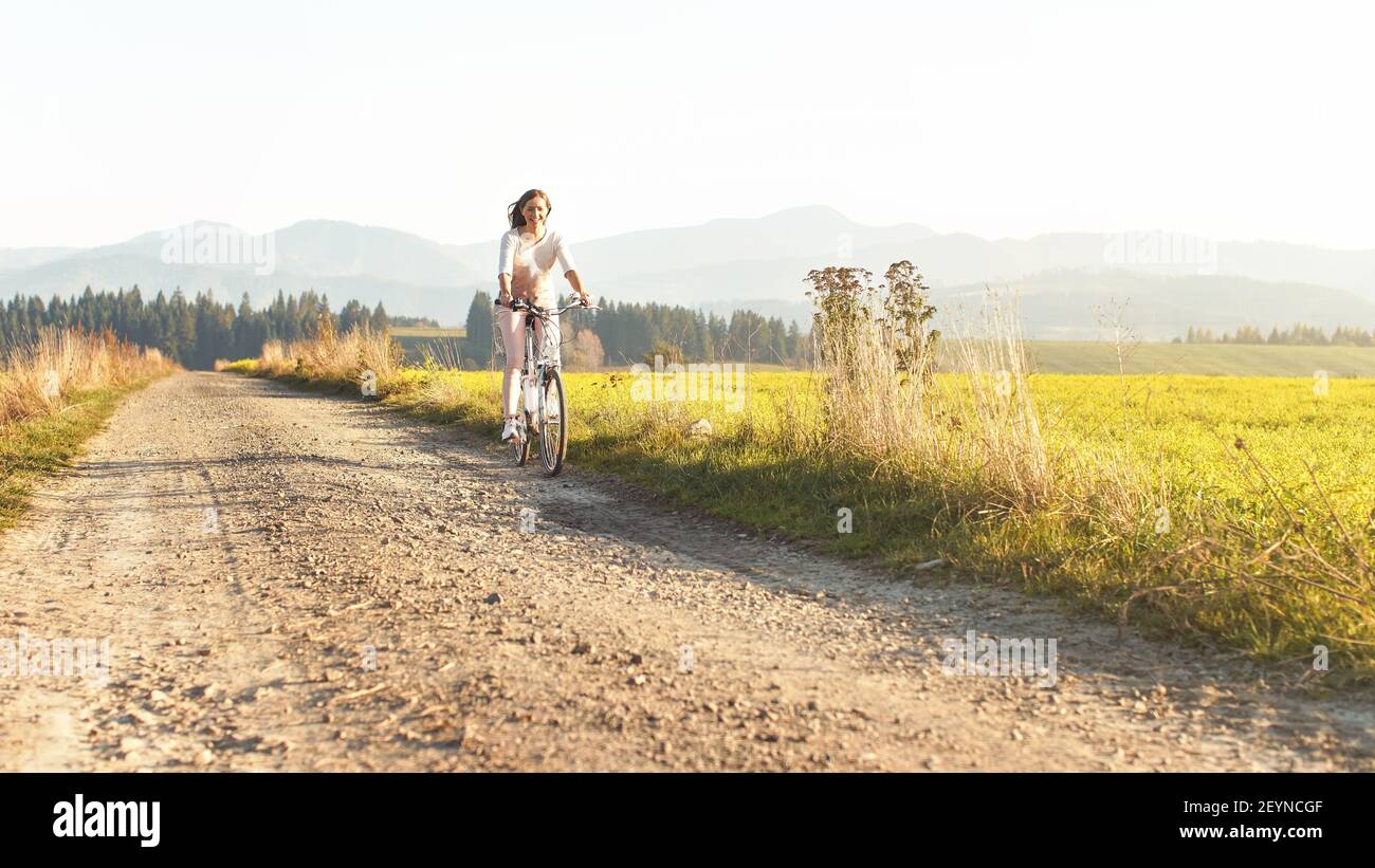 Junge Frau, die auf staubiger Straße im Freien Fahrrad fährt, sonnenbeschienenen Wiese in der Nähe Stockfoto