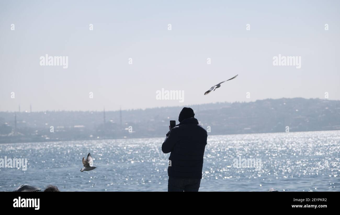 Türkei. Bosporus istanbul. Menschen, Touristen sitzen auf Betonstein in Ufer bosporus. Sie fotografieren und füttern Möwen und Tauben und Tauben Stockfoto