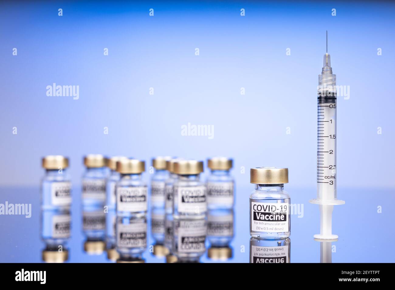 Konzentrieren Sie sich auf ein Covid-19-Impfstofffläschchen mit Spritze, mit mehreren verschwommenen Fläschchen auf blauem Hintergrund Stockfoto
