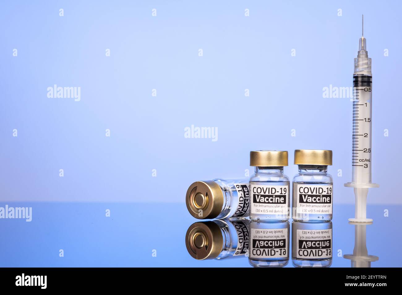 Covid-19 Impfstofffläschchen mit Spritzenkonzept auf reflektierender Oberfläche Blauer Hintergrund Stockfoto