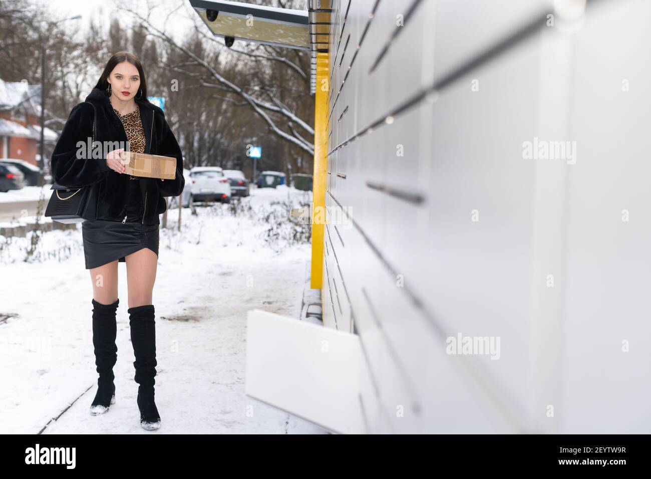 Ein attraktiver Student sammelt im Winter ein Paket über einen Paketschrank ein und schickt es. Automatische Maschine zum Senden und Empfangen von Briefen und Paketen. Stockfoto