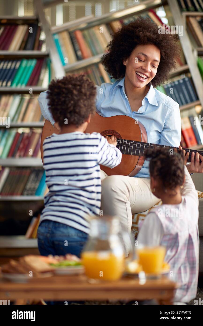 Mama mit Kindern spielt gerne Gitarre in entspannter Atmosphäre zu Hause. Familie, zusammen, Liebe, Spielzeit Stockfoto