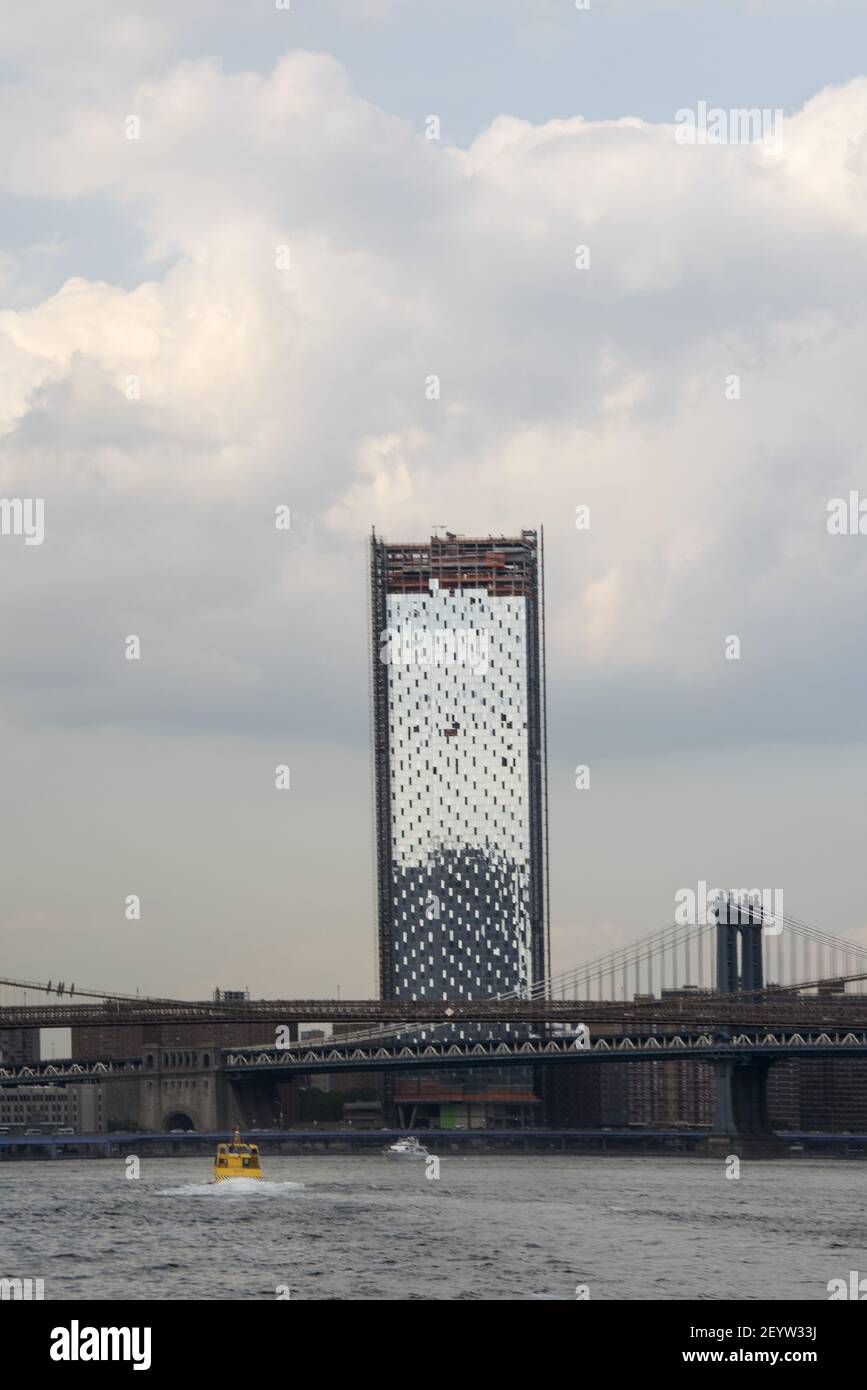 Eine gelbe Wasserfähre fährt den East River von NYC hinauf und nähert sich einem hohen Gebäude und der Manhattan Bridge. Stockfoto