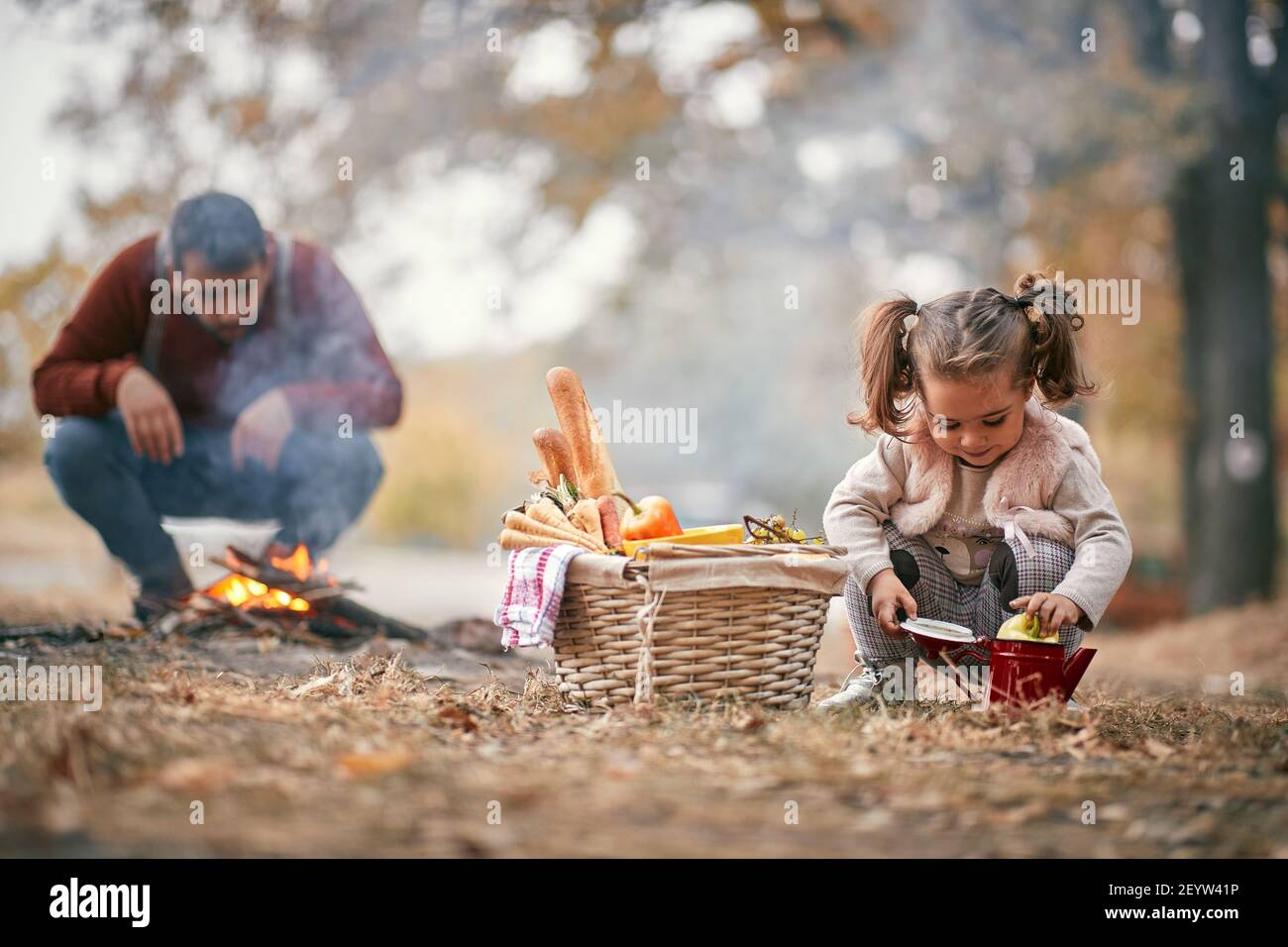 Kleines Mädchen auf Picknick spielen, während Vater das Feuer vorbereitet Stockfoto