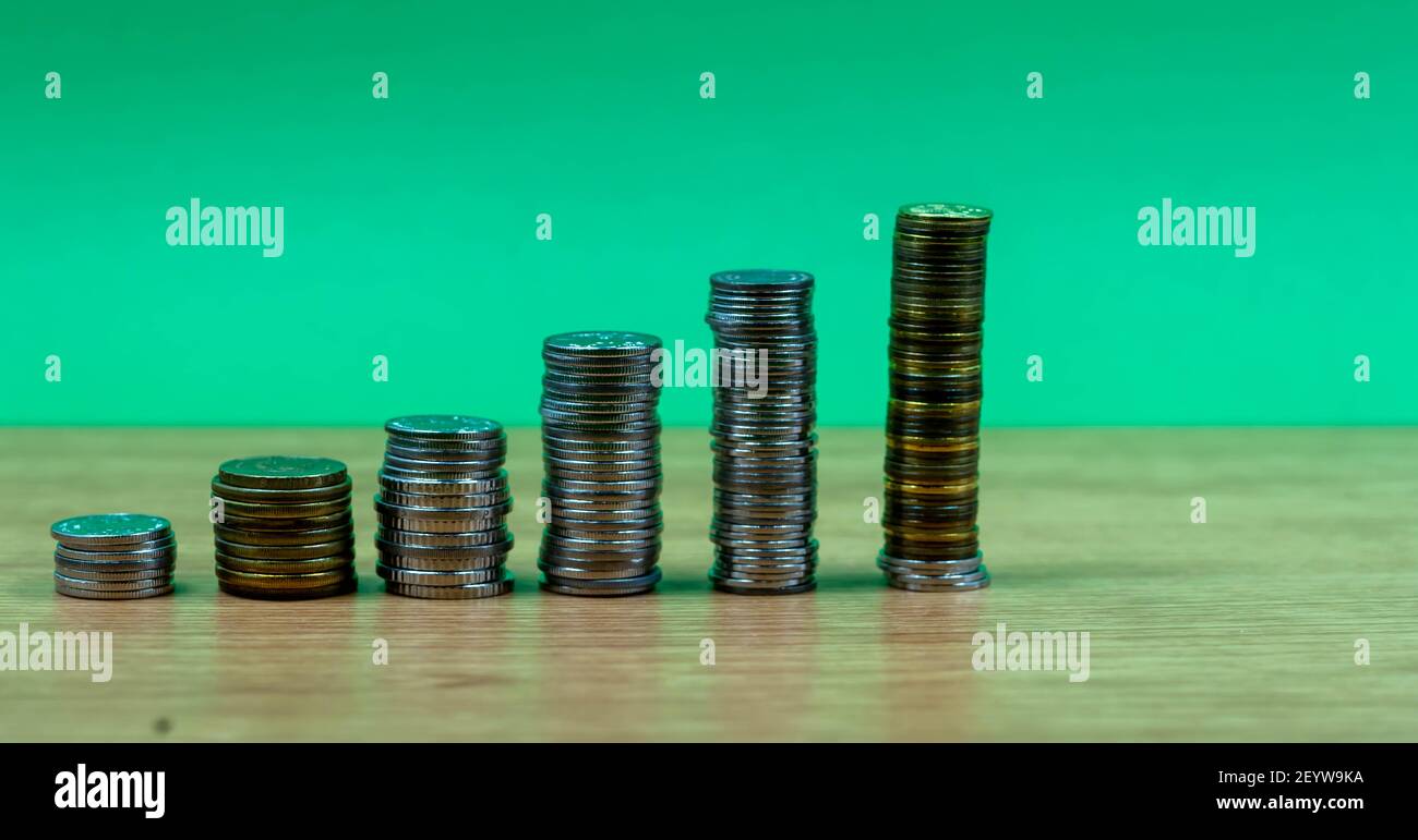 Ersparnisse, zunehmende Spalten von Gold und Silber Münzen isoliert auf grünem Hintergrund Stockfoto