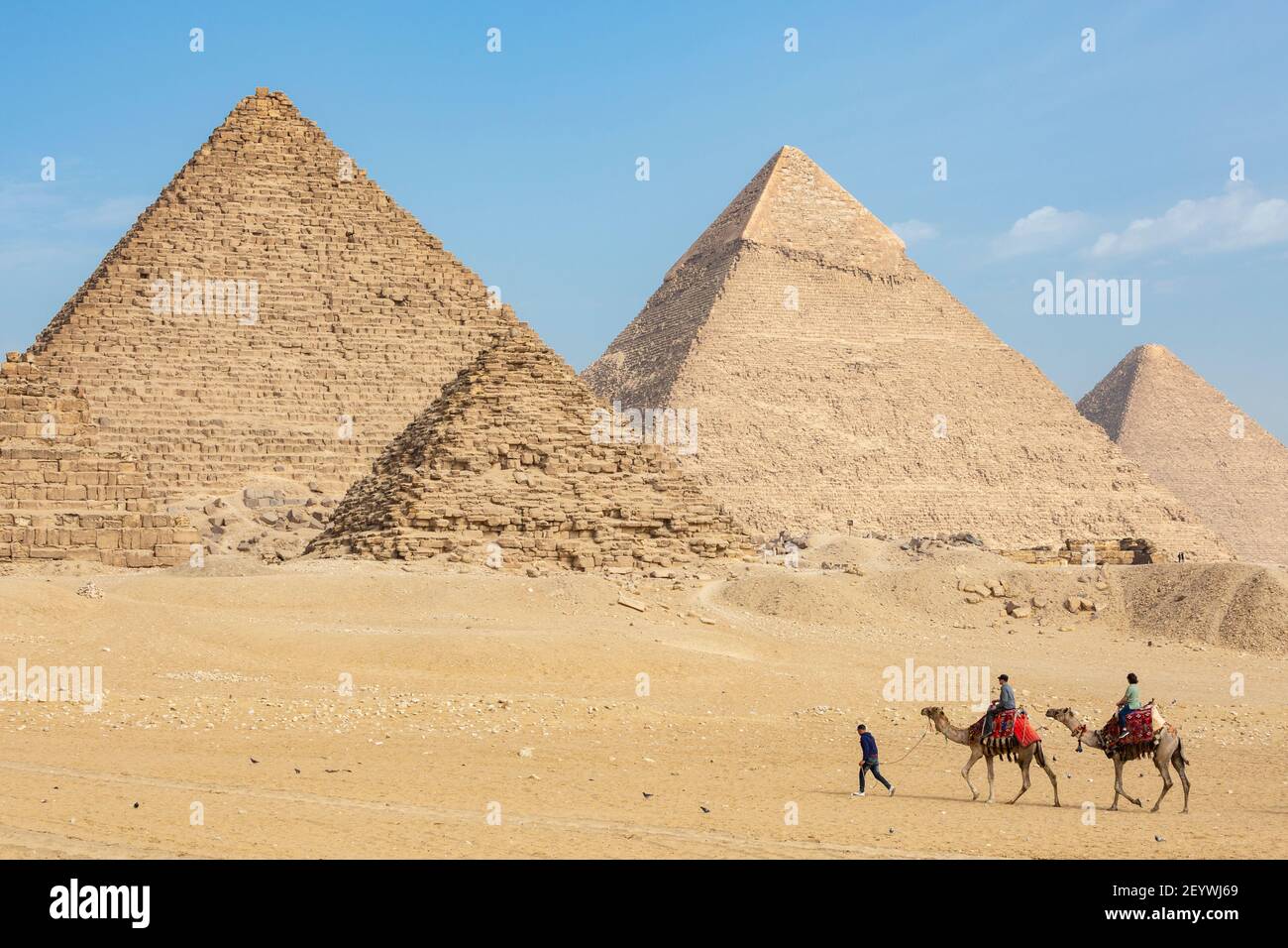 Ein lokaler Reiseleiter führt zwei Touristen auf Kamelen um die Pyramiden von Gizeh, Gizeh Plateau, Groß-Kairo, Ägypten Stockfoto