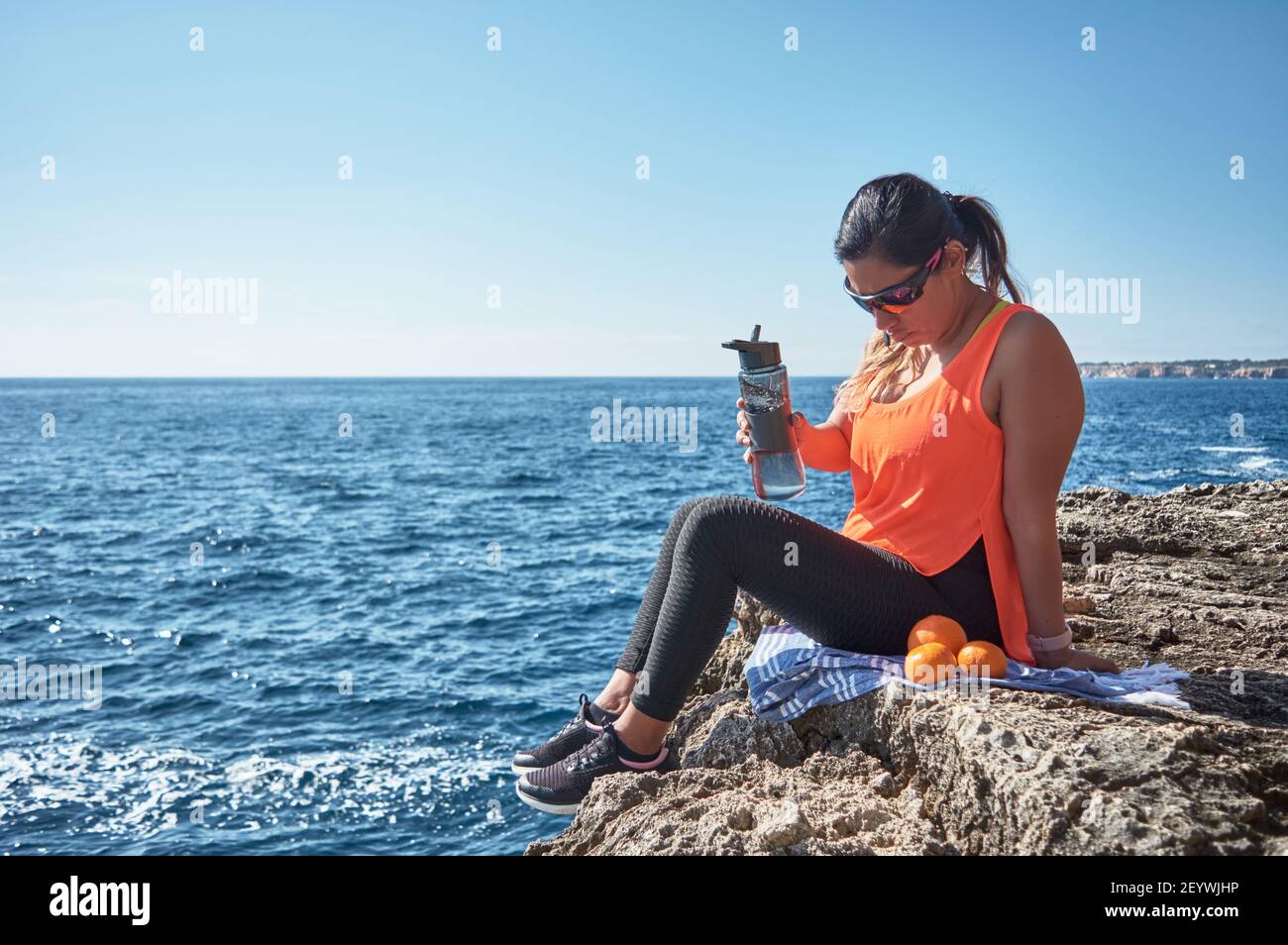 Lateinische Frau, mittleren Alters, ausruhen, Kraft zurückgewinnen, essen, Trinkwasser, nach einem Fitness-Studio-Sitzung, Kalorien zu verbrennen, fit zu halten, im Freien am Meer Stockfoto